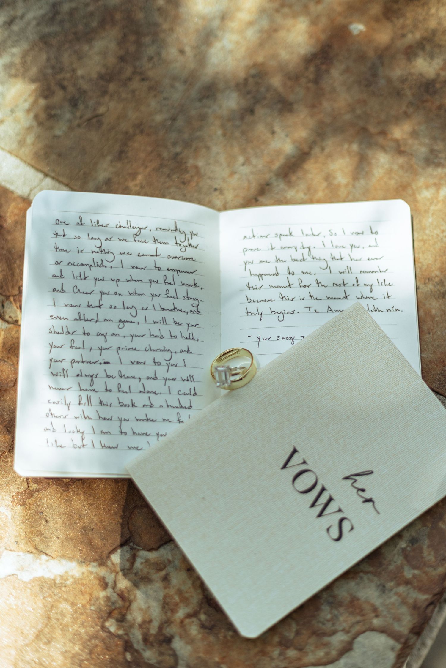 Handwritten wedding vows on white paper with wedding rings placed on textured stone surface.