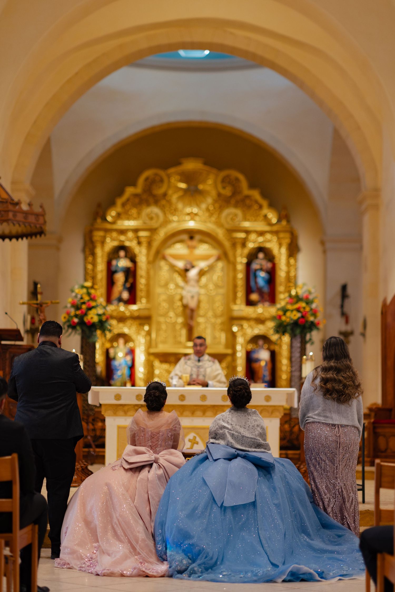 Ornate Catholic church altar serves as backdrop for ceremony with attendees in formal attire.