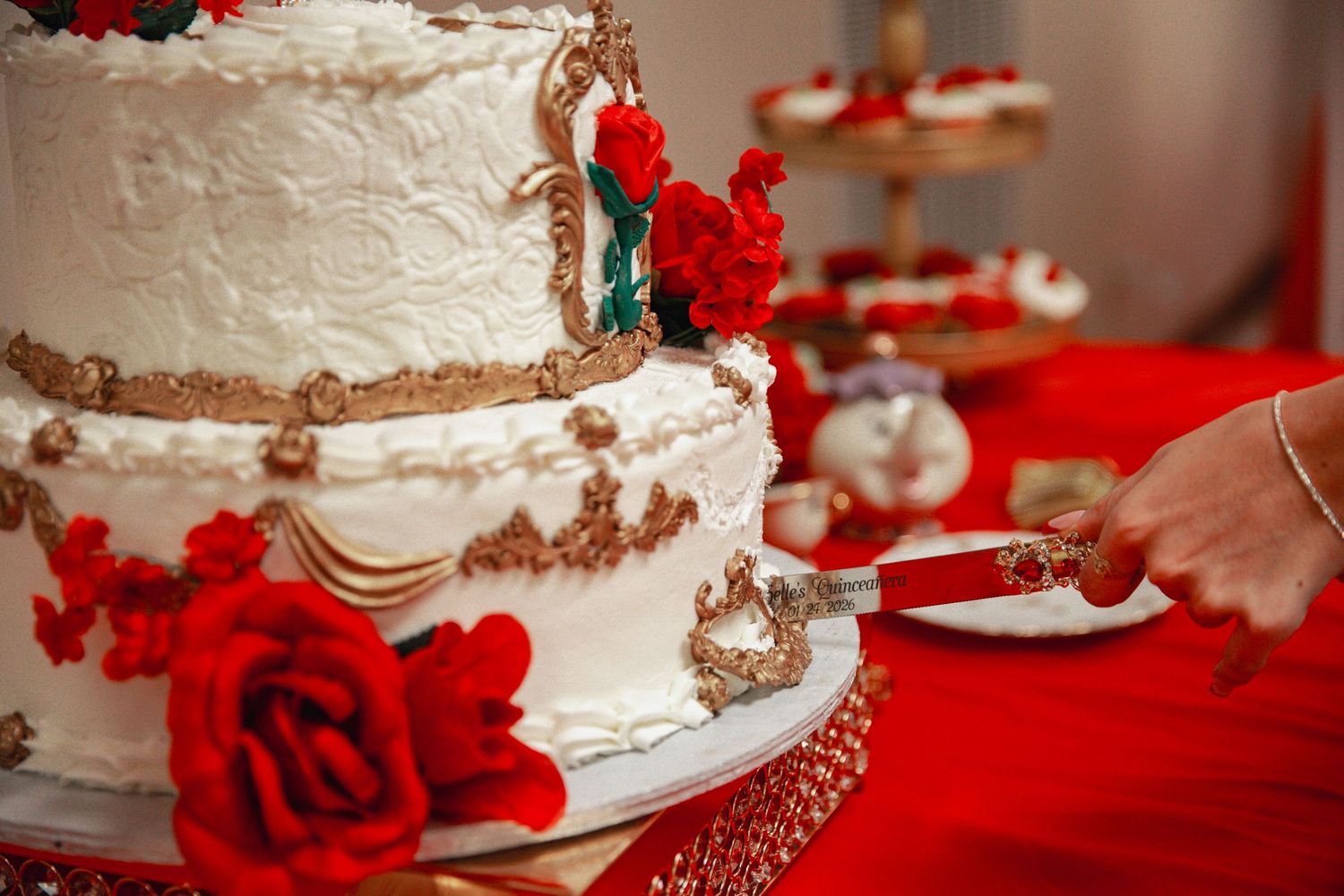 White wedding cake decorated with red roses on a red tablecloth.