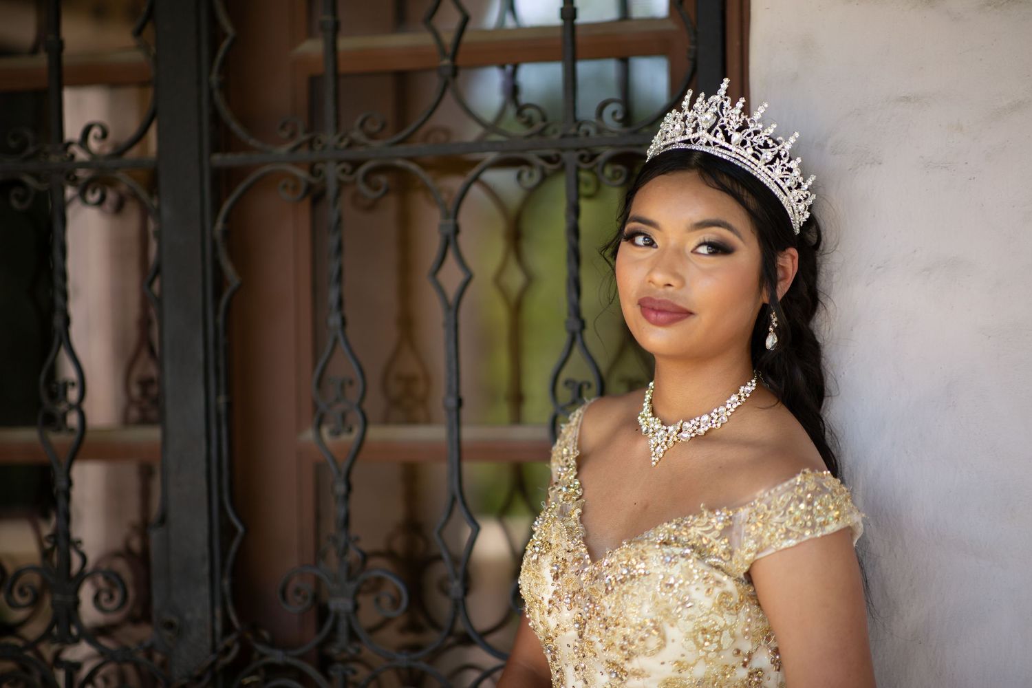 Ornate cream and gold ballgown photographed against neutral wall with decorative ironwork.
