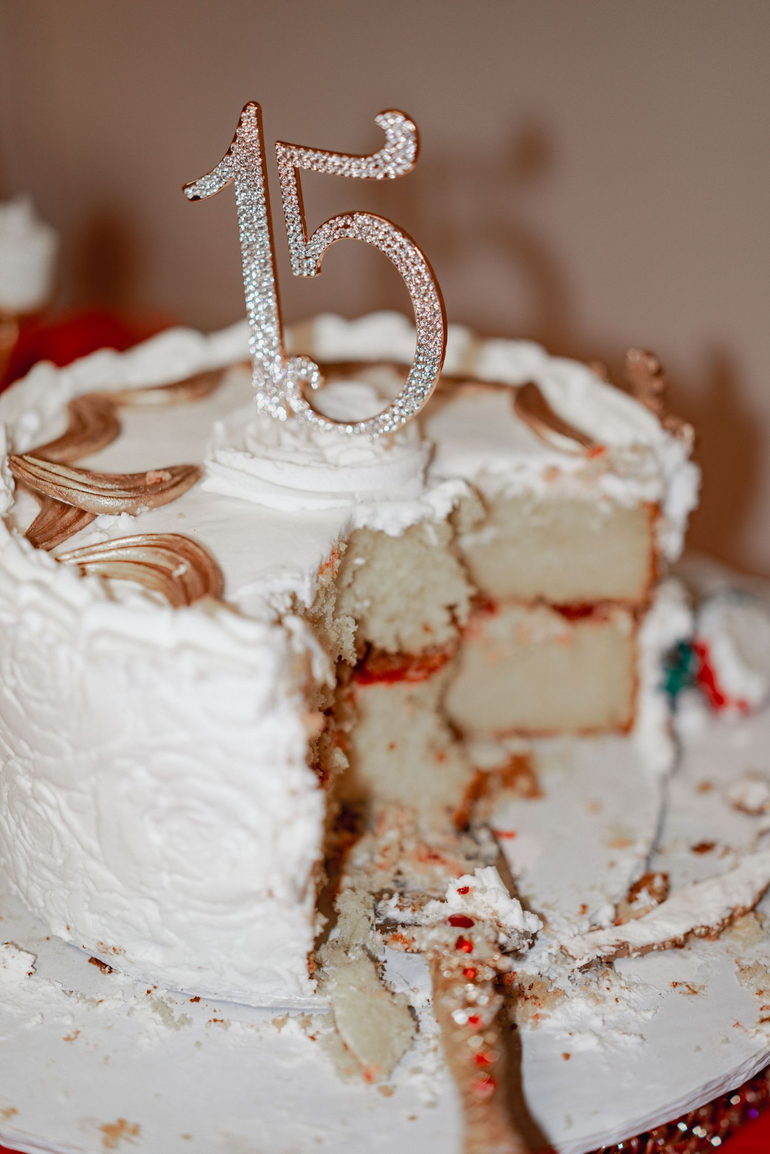 A partially eaten white birthday cake with silver number 15 topper and decorative details.