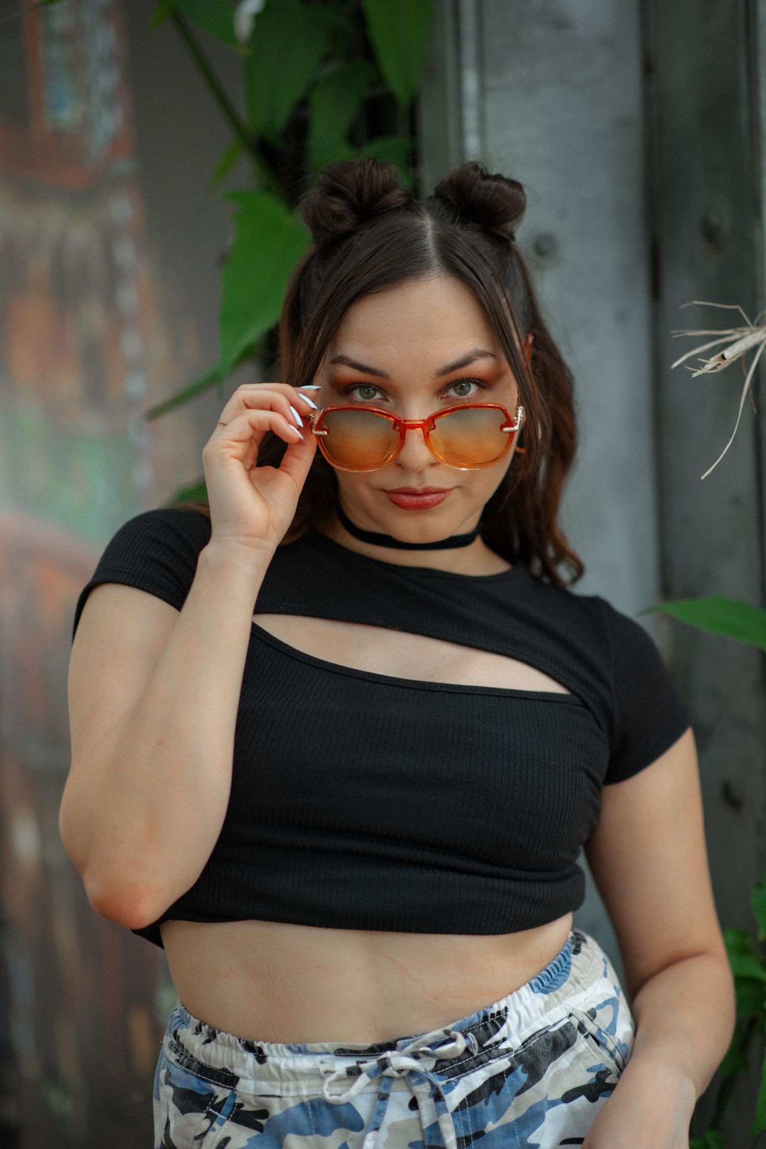 Fashion portrait with orange sunglasses and black crop top against urban background.