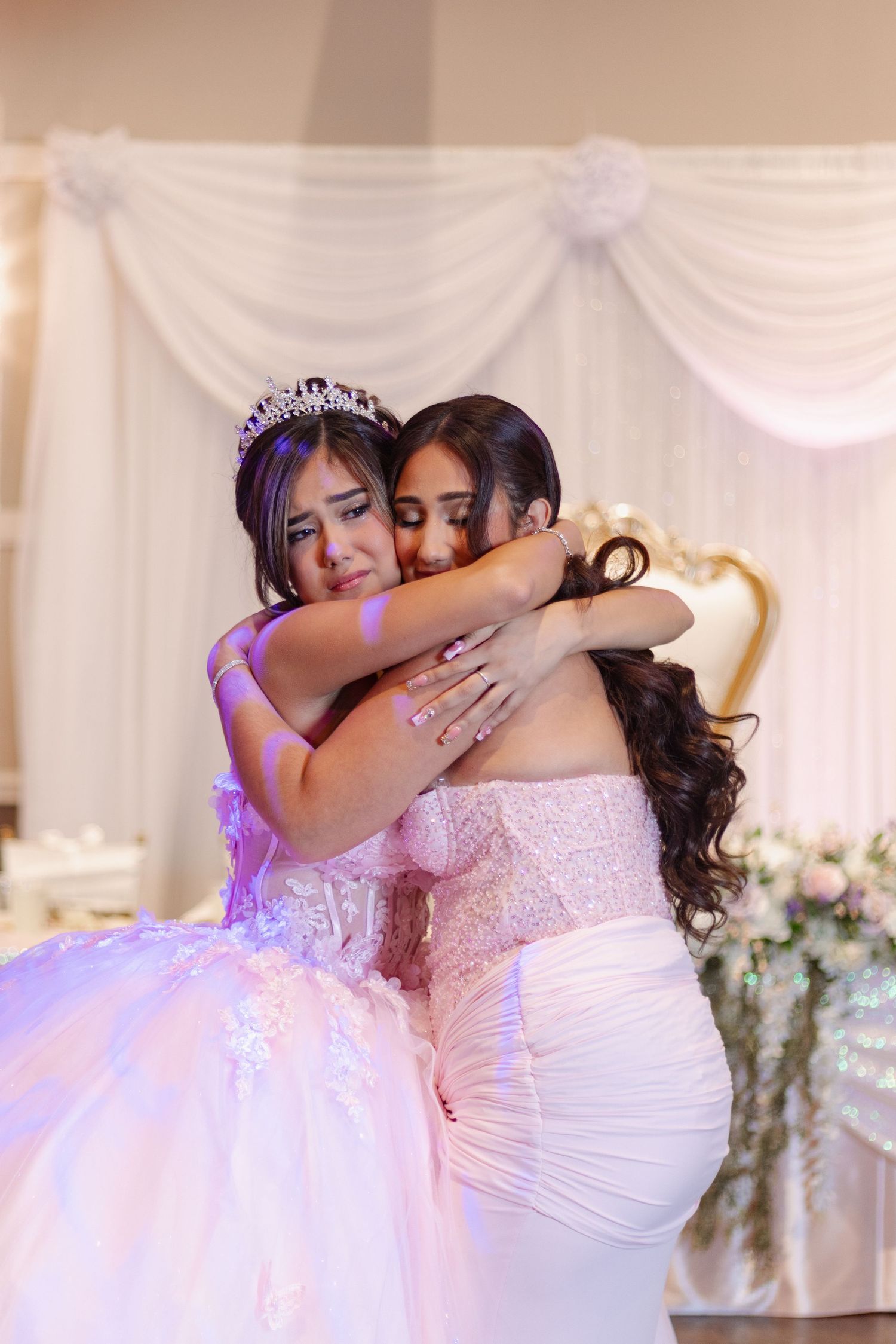 Emotional embrace between two people in white formal dresses at wedding reception.