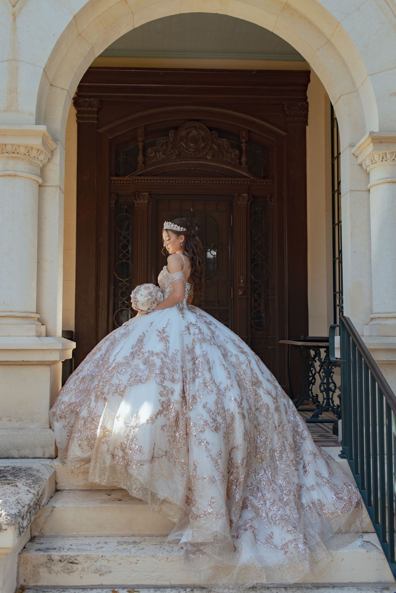 White ballgown with intricate gold detailing photographed in a classical columned setting.
