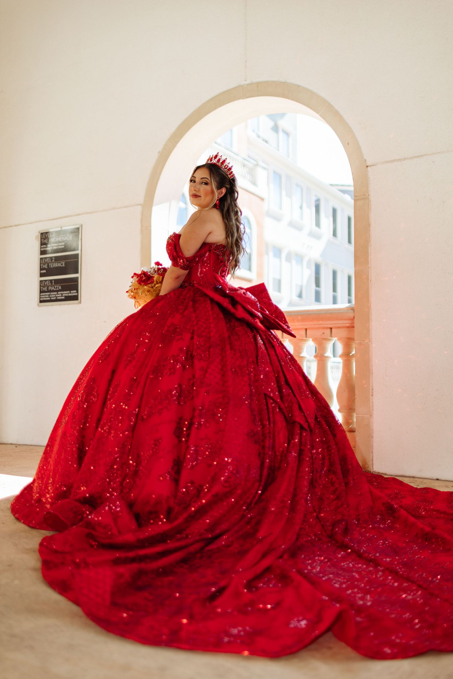 A dramatic red ball gown with sweeping train photographed under an elegant archway.