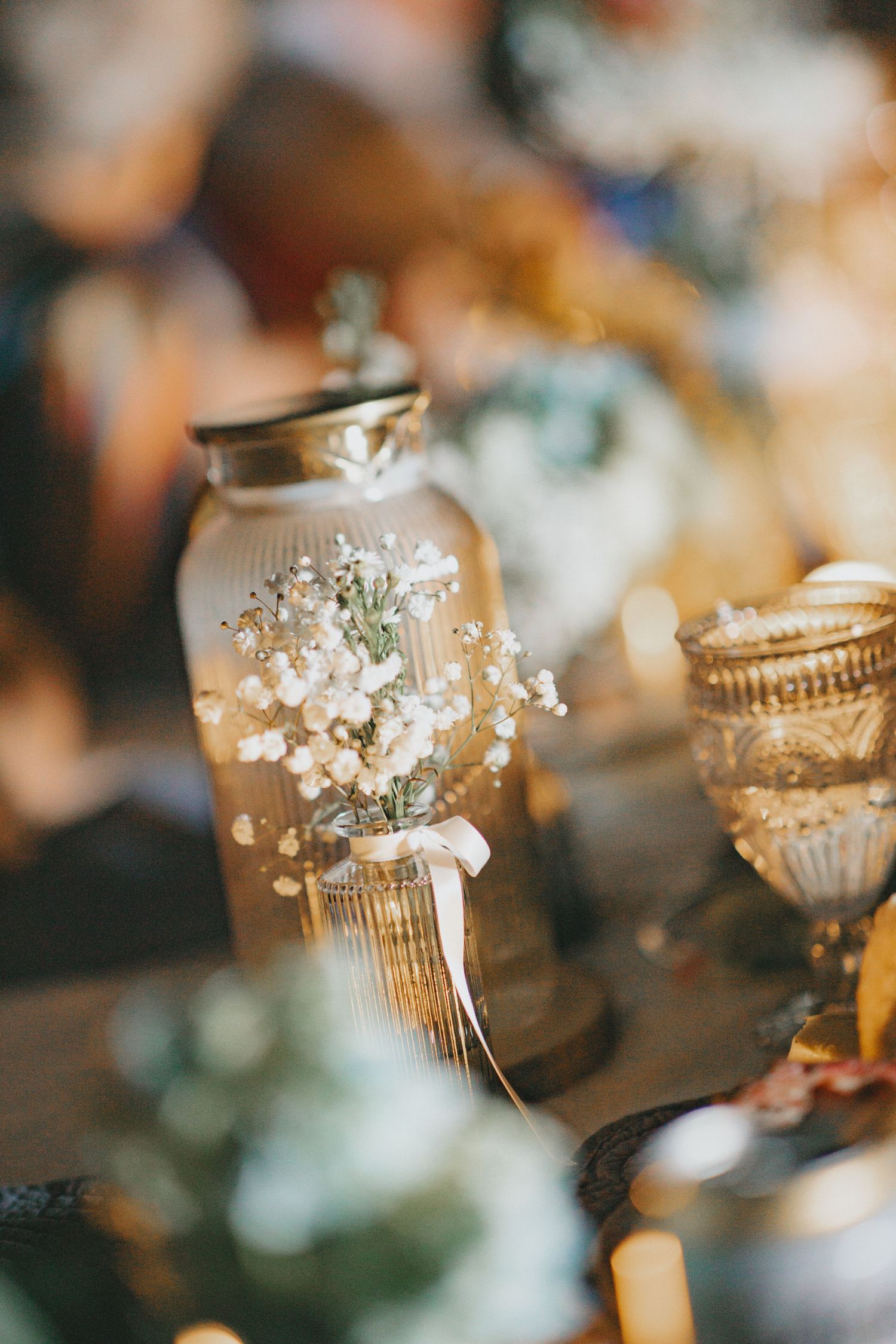 Delicate glass votive holders decorated with baby's breath flowers for wedding reception.