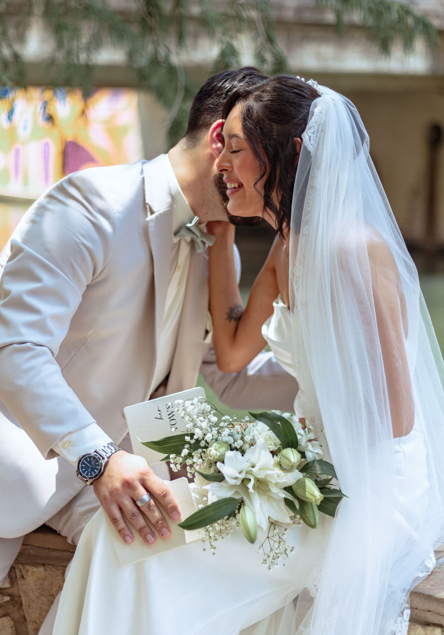 A joyful wedding portrait with white floral bouquet and elegant bridal veil against colorful backdrop.