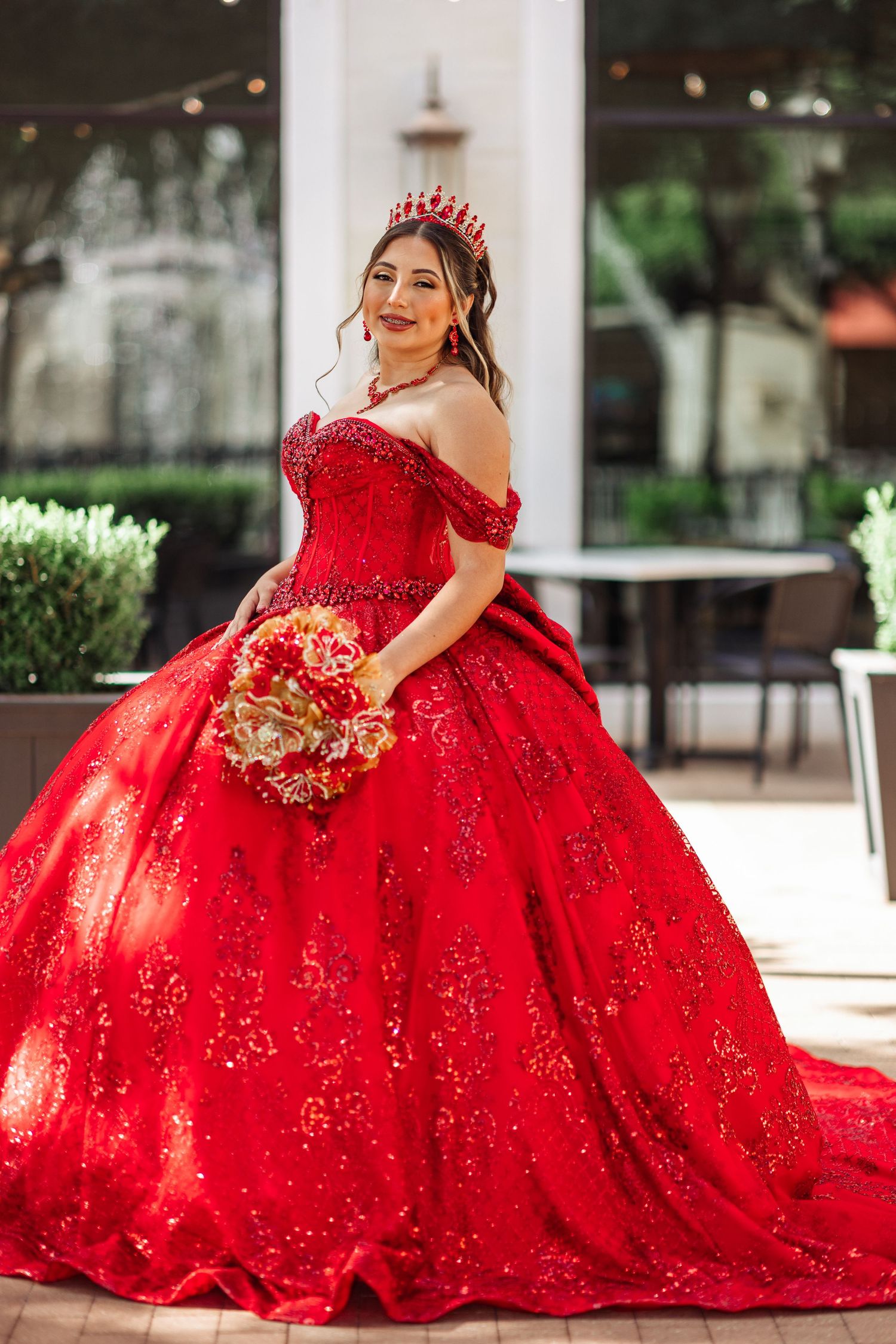 Vibrant red sequined ballgown with off-shoulder design photographed in an outdoor setting.