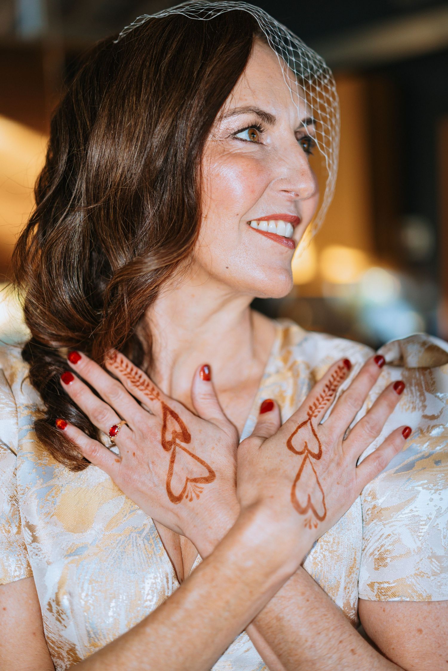 Hands decorated with henna designs shown against a white lace background.