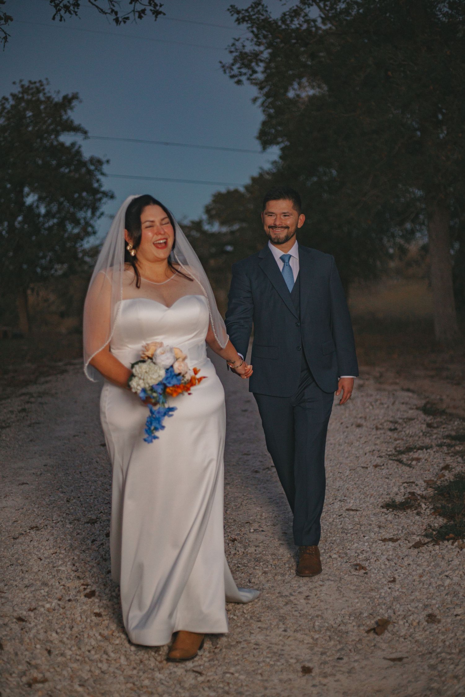 Couple walks together on gravel path during sunset wedding photoshoot.