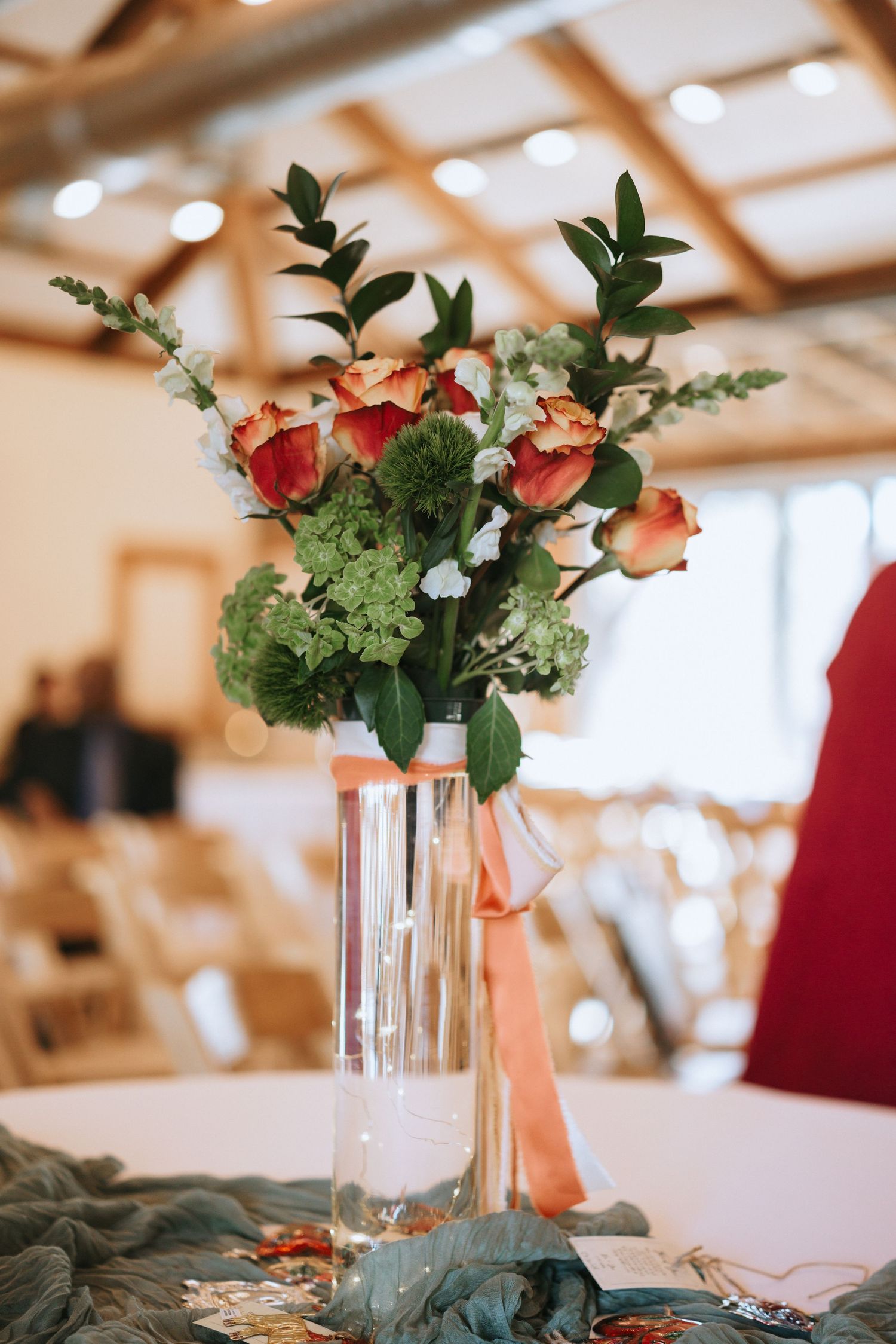 Elegant floral centerpiece with coral and white flowers in a tall glass vase on a wedding reception table.