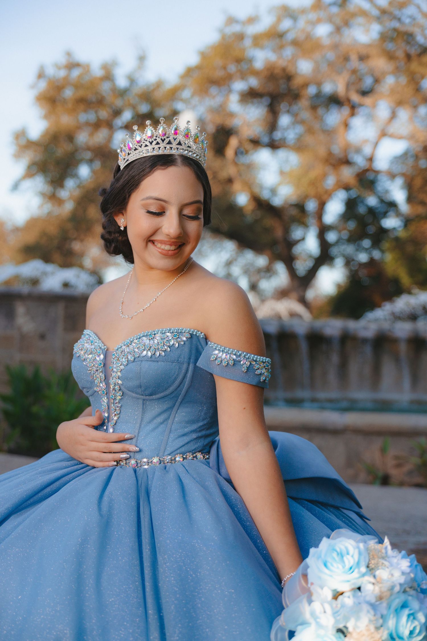 Powder blue ball gown with crystal embellishments and off-shoulder design captured in golden hour light.