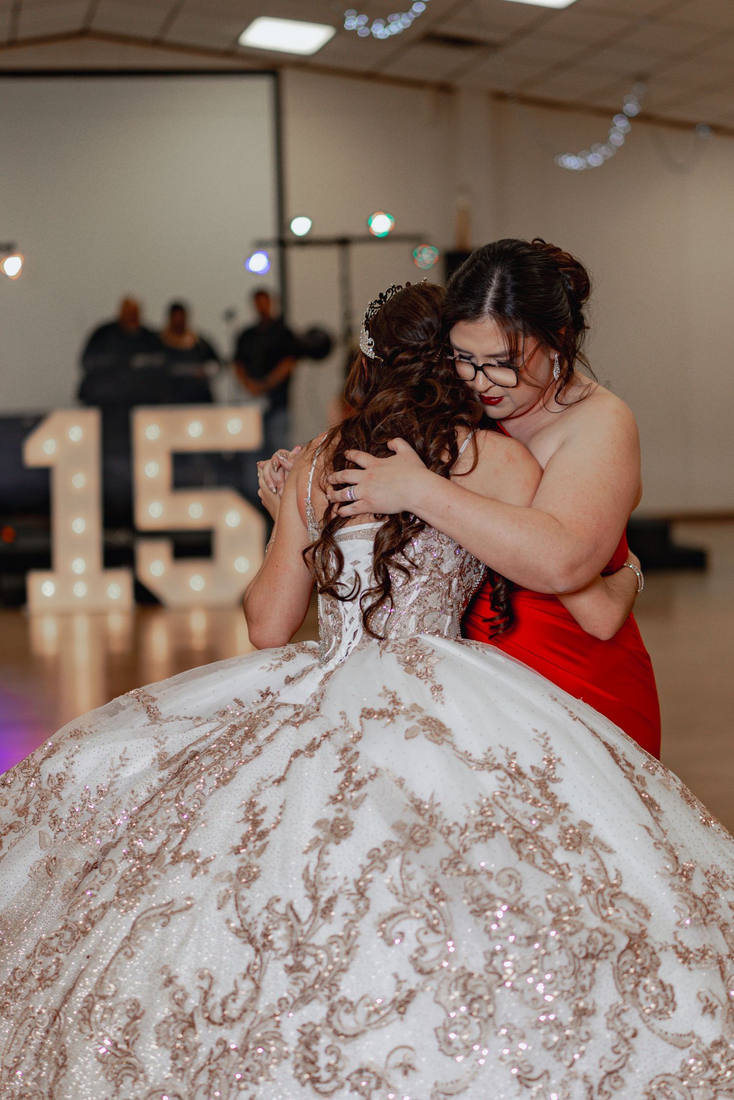 A heartfelt moment captured between two people, one in a sparkly white ballgown and another in vibrant red.