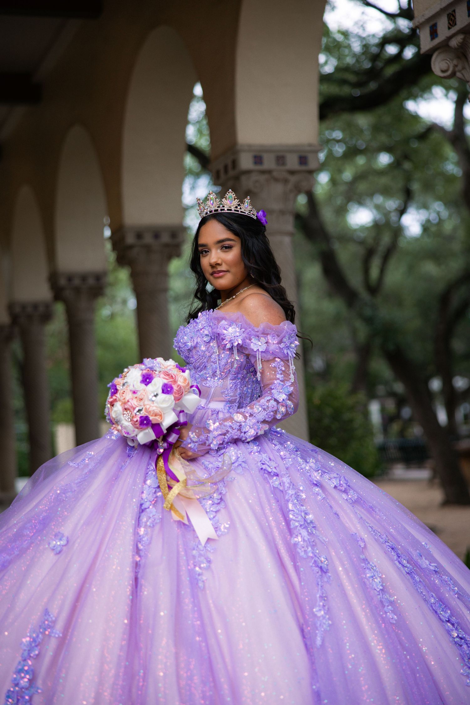 Ethereal purple ball gown with floral details and crystal embellishments in a columned courtyard.