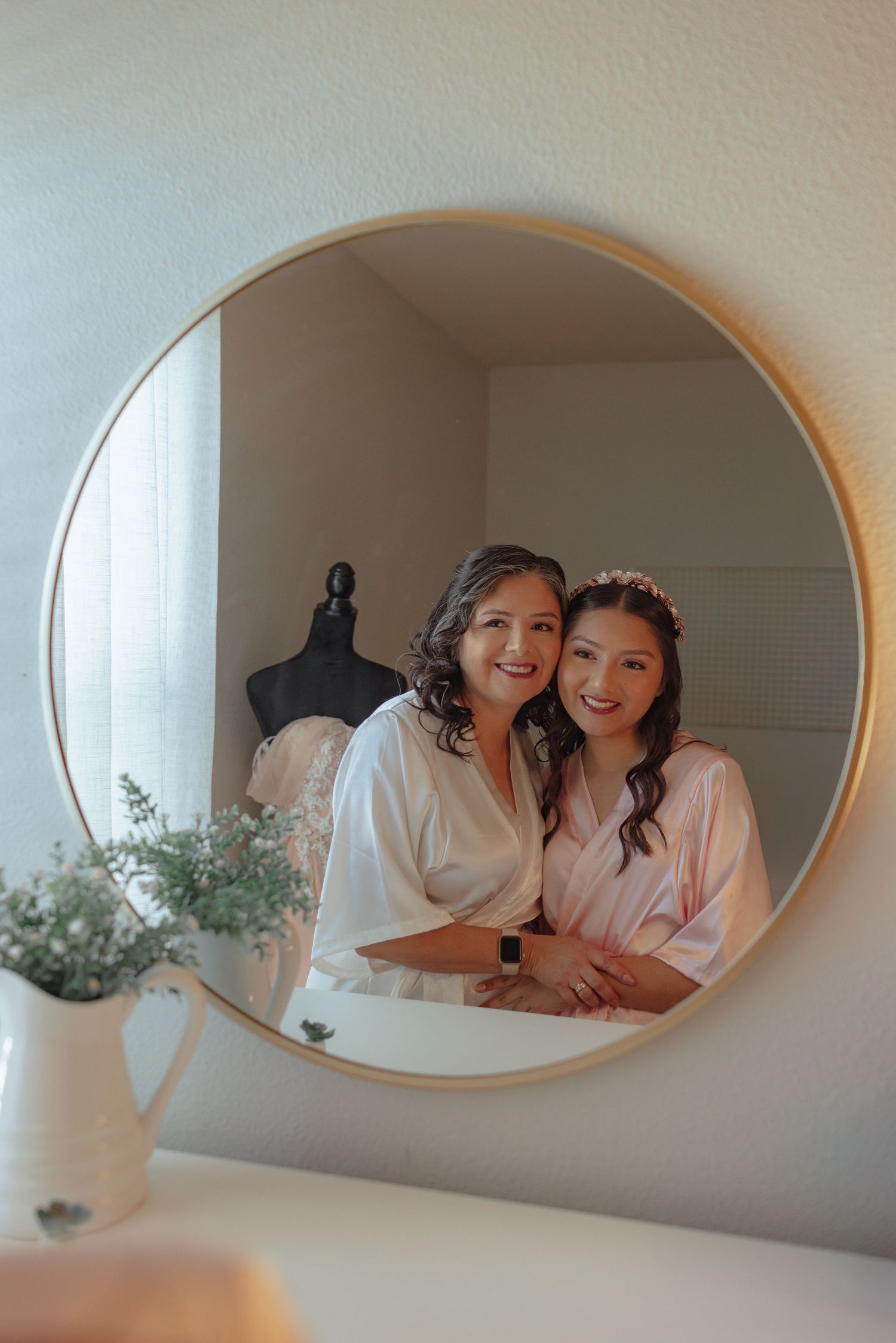 Getting ready scene reflected in oval mirror with bridesmaids in matching robes.
