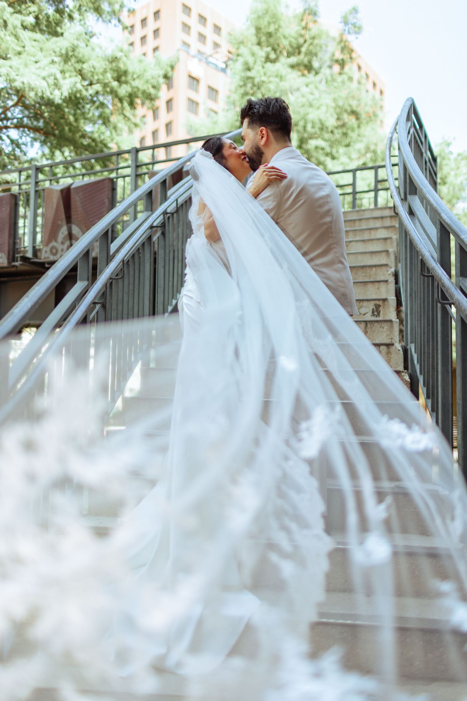 Newlyweds share intimate moments on an outdoor staircase with flowing white wedding dress details.