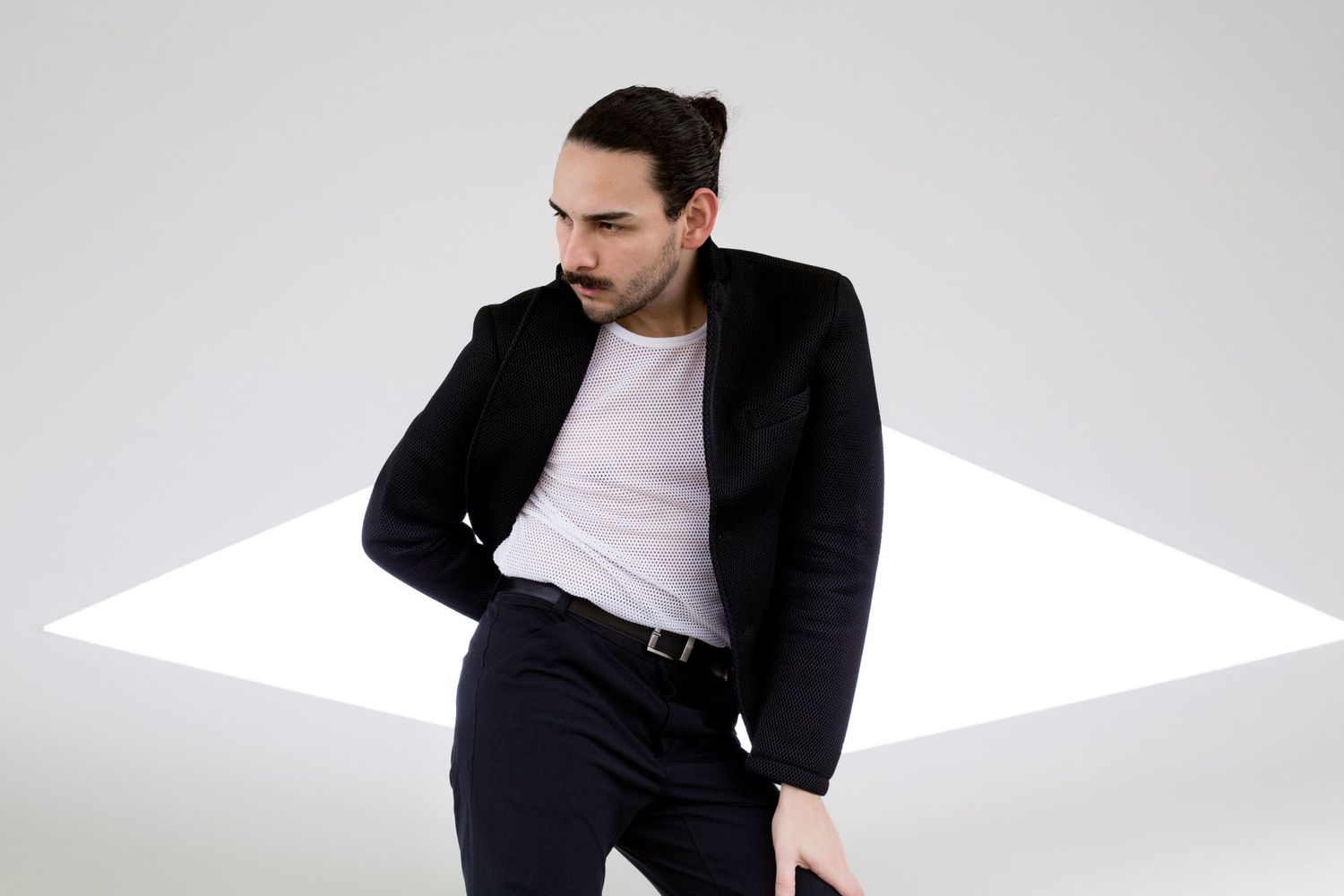 Man in black suit and white shirt posing against white background in modern fashion shoot.