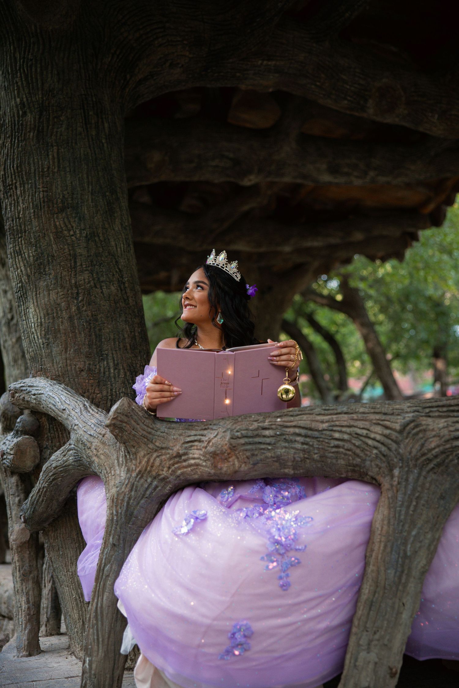 Lavender quinceañera dress displayed outdoors among tree branches in natural lighting.