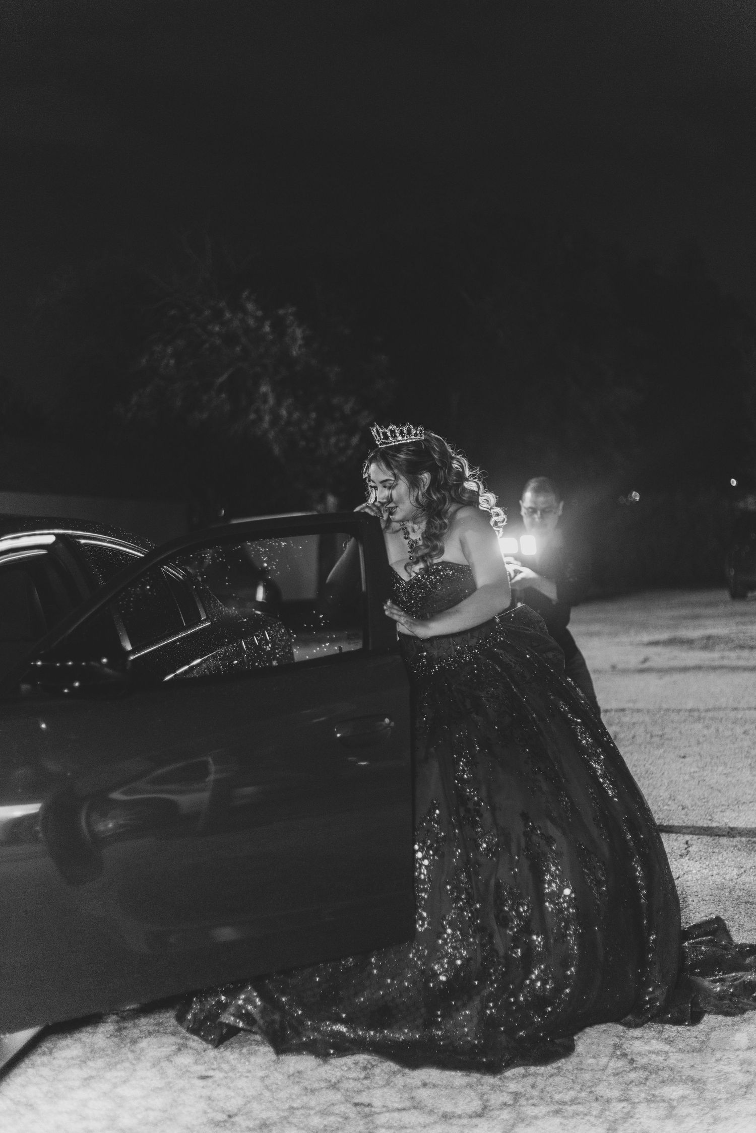 Nighttime photo of a sparkling black gown against car headlights.