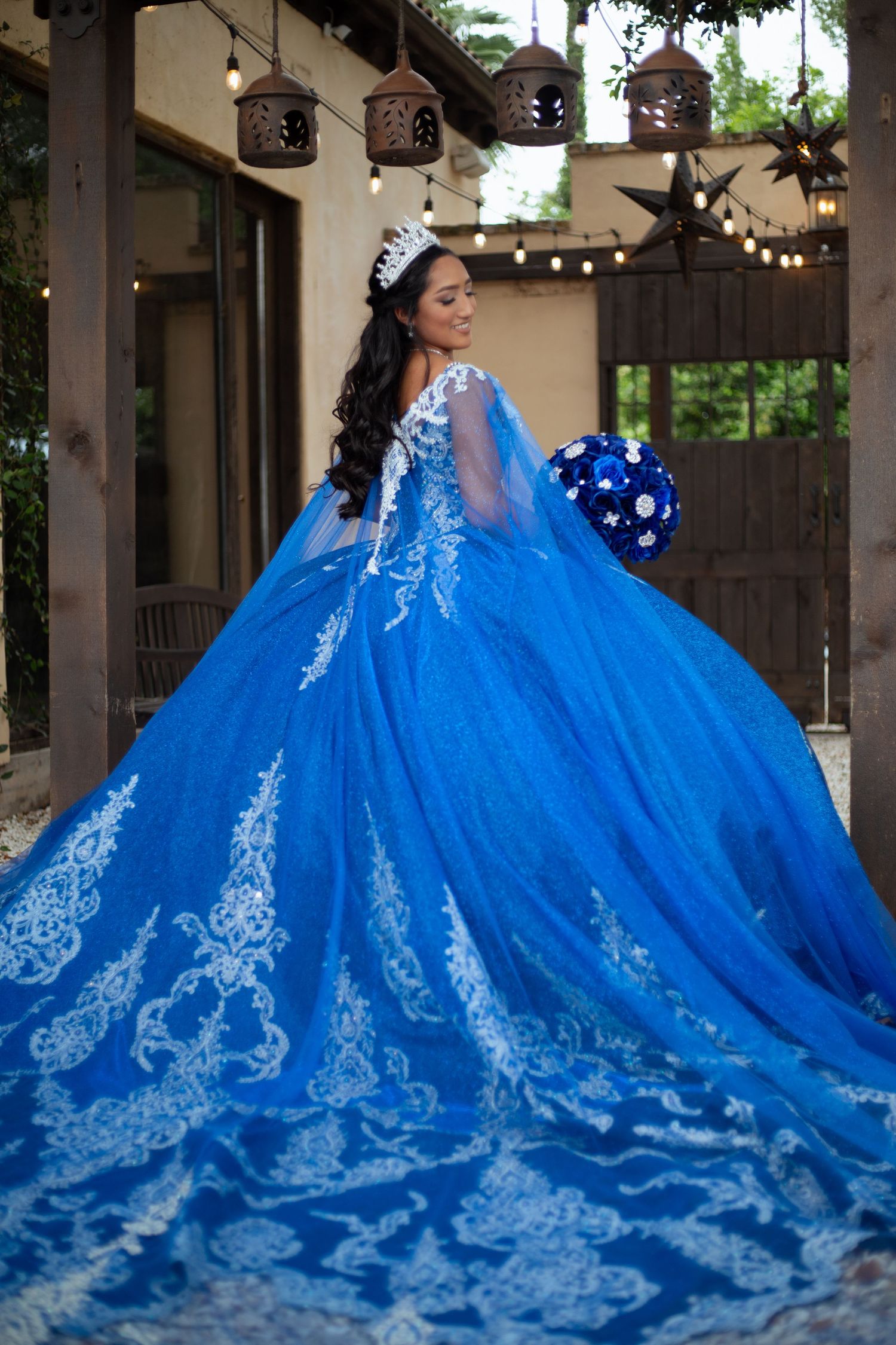 Stunning royal blue ball gown with intricate white lace details flows across outdoor patio.