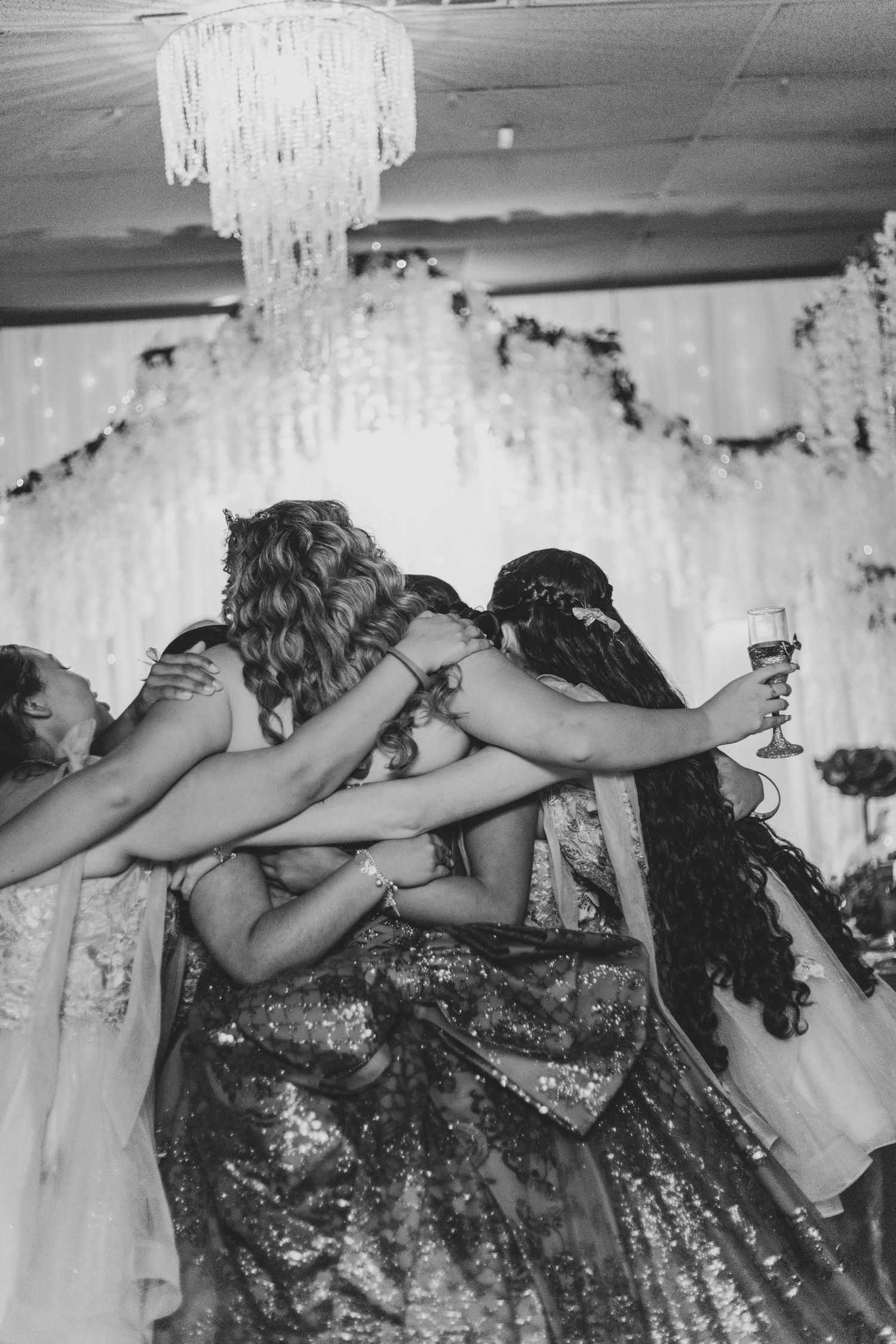 Black and white photo of friends huddled together in celebration with raised glasses.