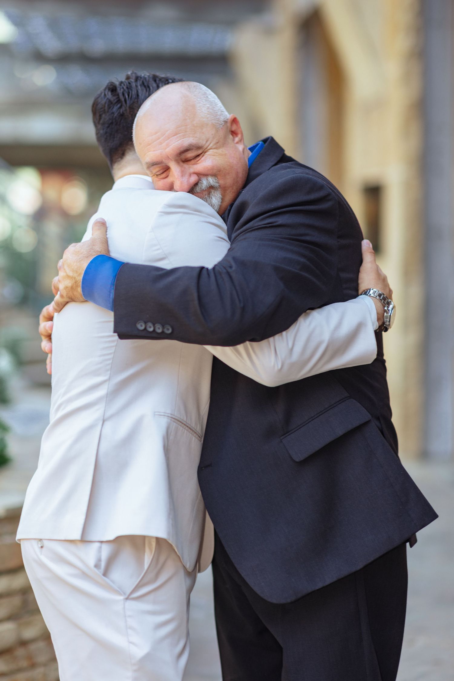Emotional embraces shared between men in formal attire at a wedding celebration.