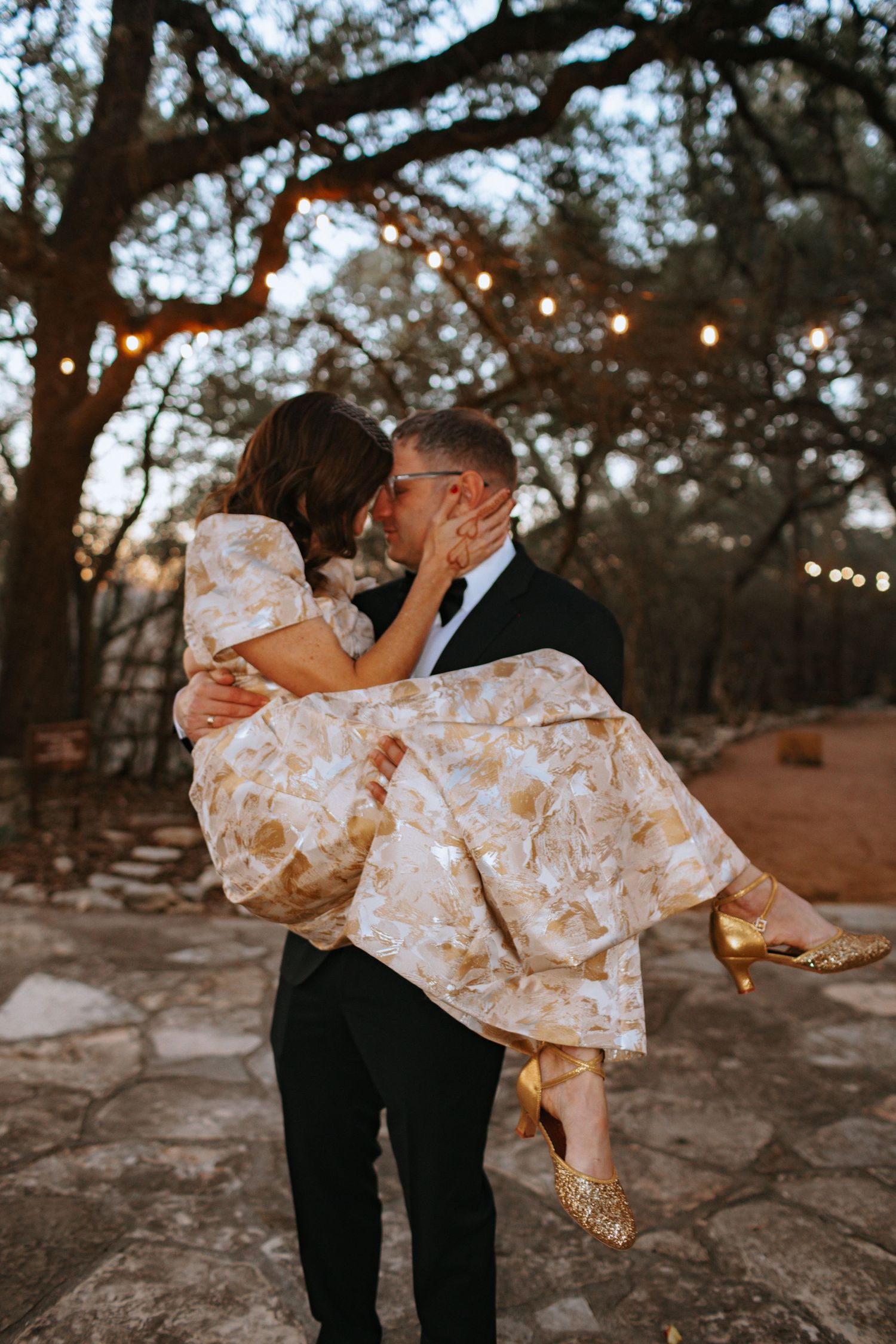 Couple dancing outdoors with string lights and trees in background.