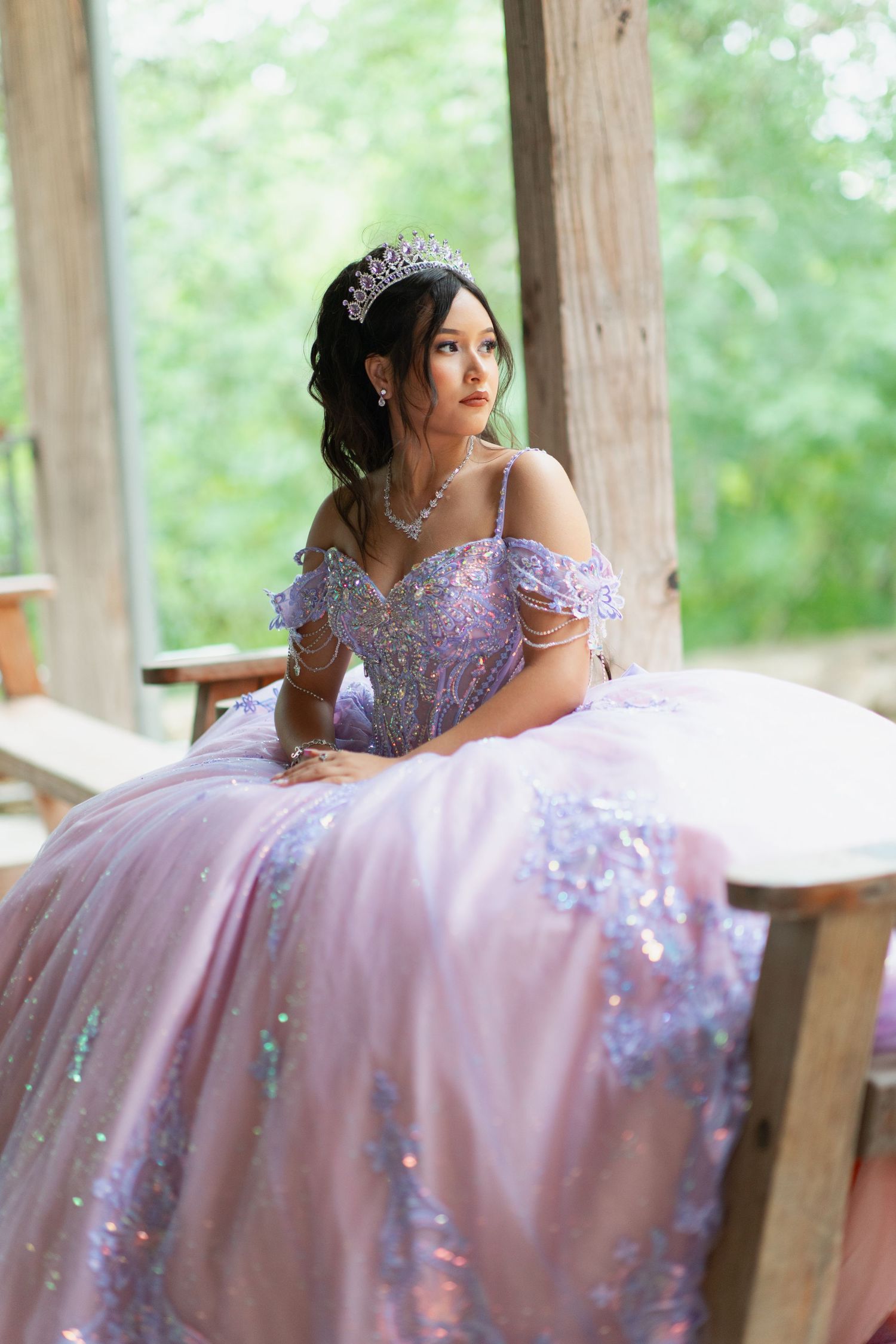 A romantic portrait of a pink and purple ball gown with off-shoulder details in a wooden gazebo.