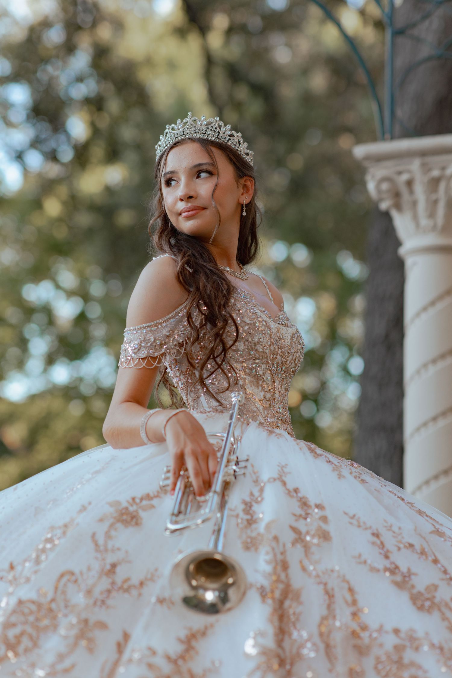 Ornate white quinceañera dress with rose gold accents photographed near classical columns.