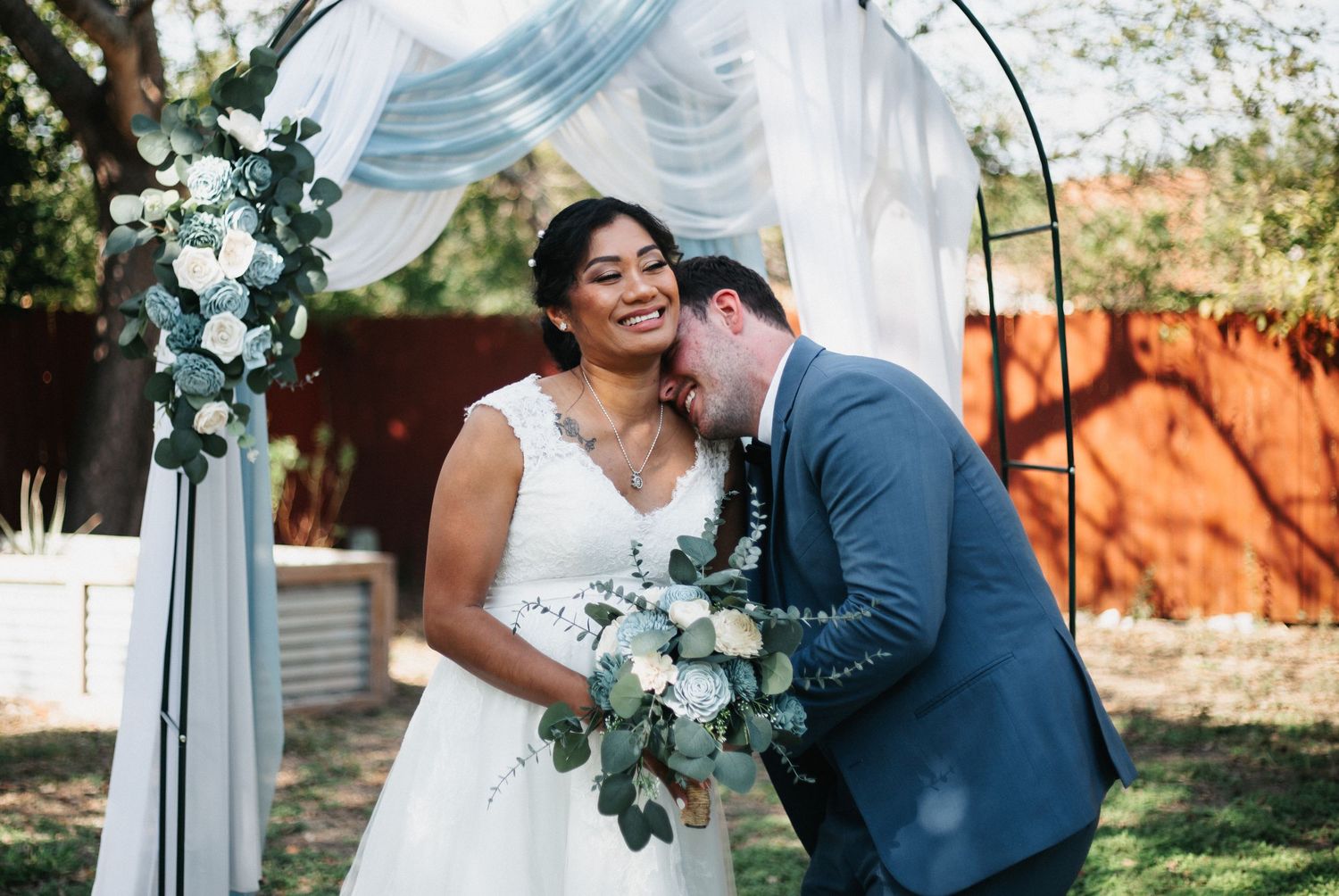 Joyful wedding moment under a floral arch with eucalyptus and white fabric draping.