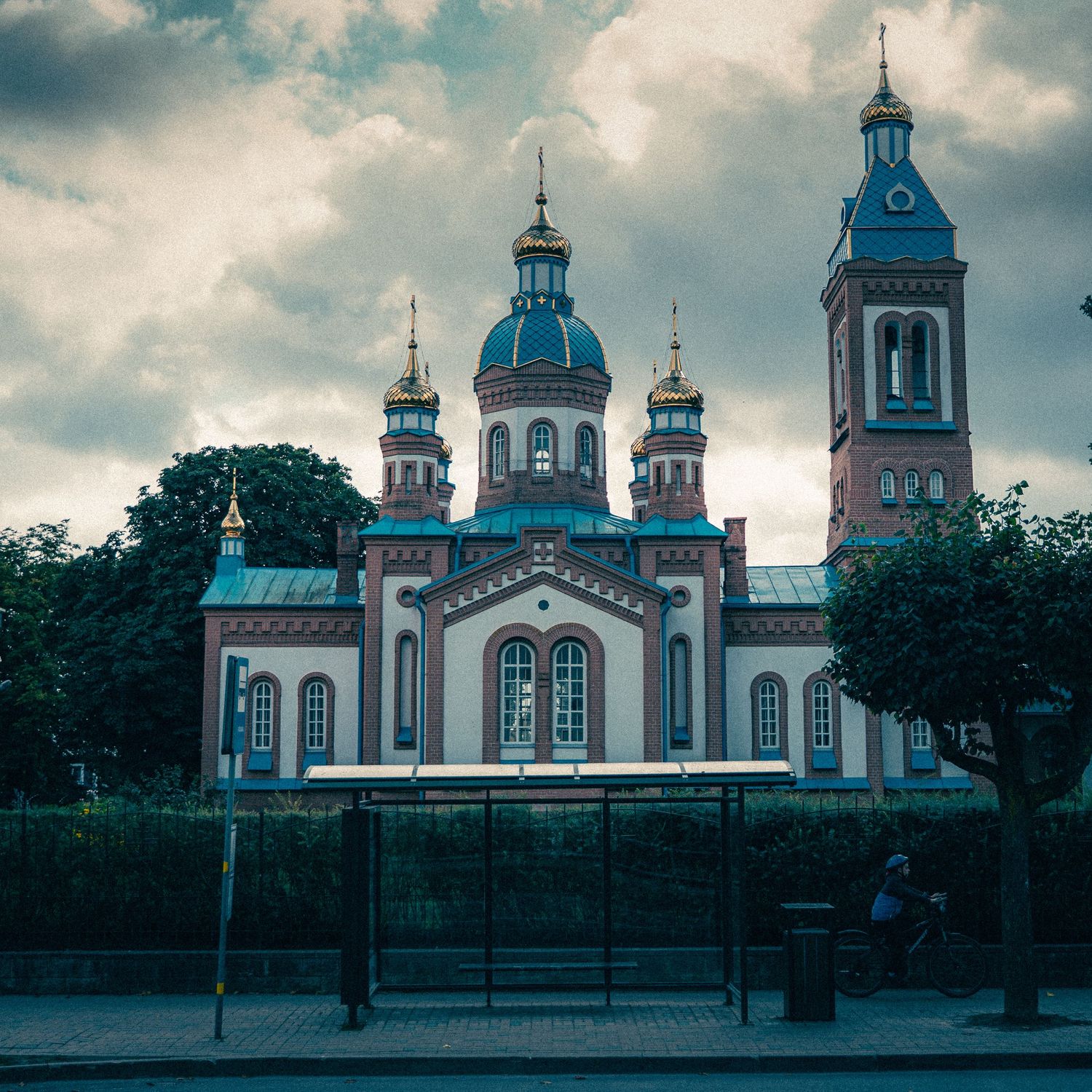 Historic church buildings with blue domes and white walls stand against a cloudy sky in panoramic view.