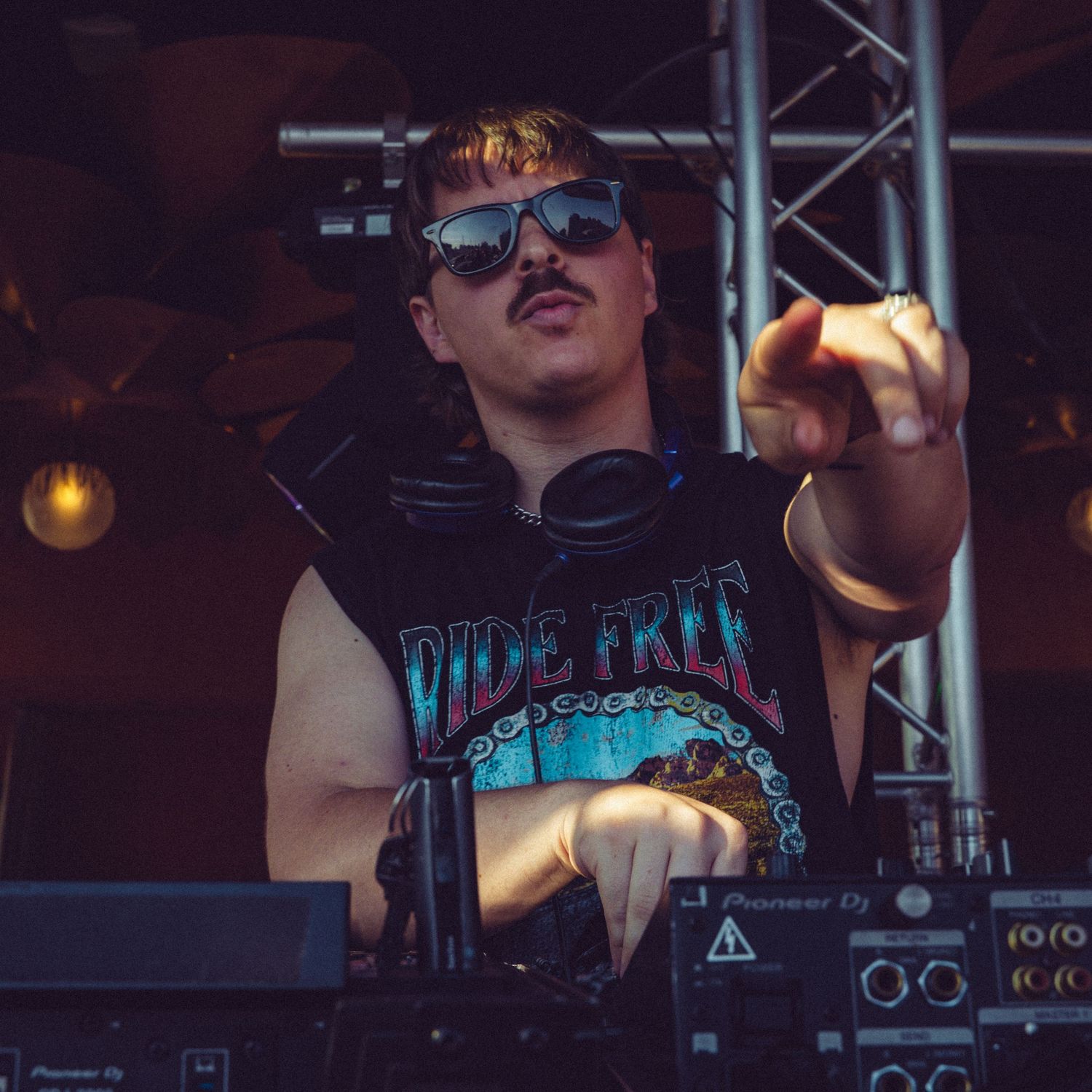 DJ performing with electronic music equipment under blue stage lighting.