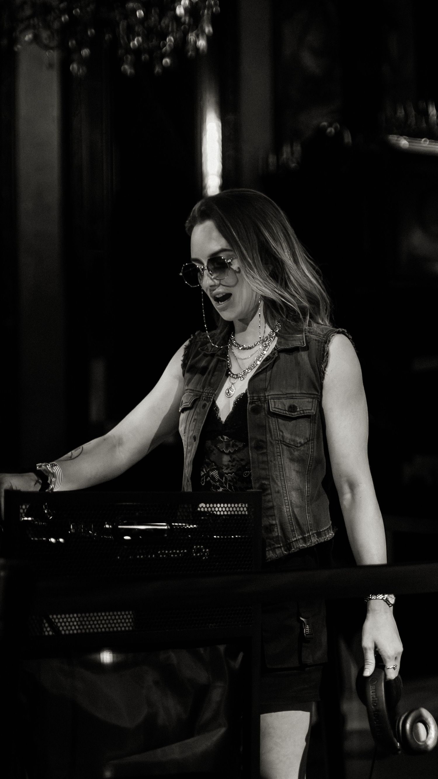 Person in a denim vest performing at a dimly lit venue.