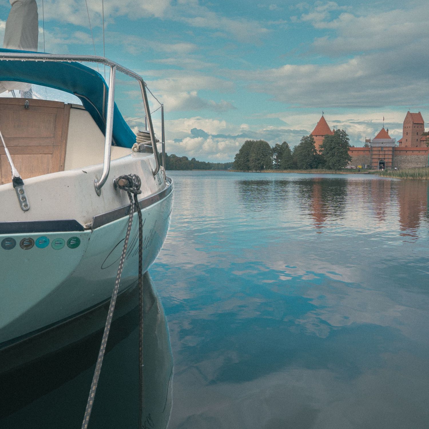 Close-up view of moored boats reflecting in calm blue waters with castle towers visible in background.