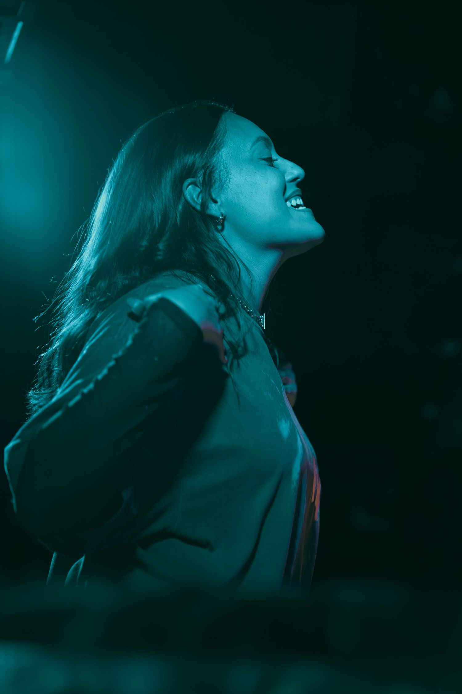 Concert performer in dramatic blue-green stage lighting during an energetic performance.