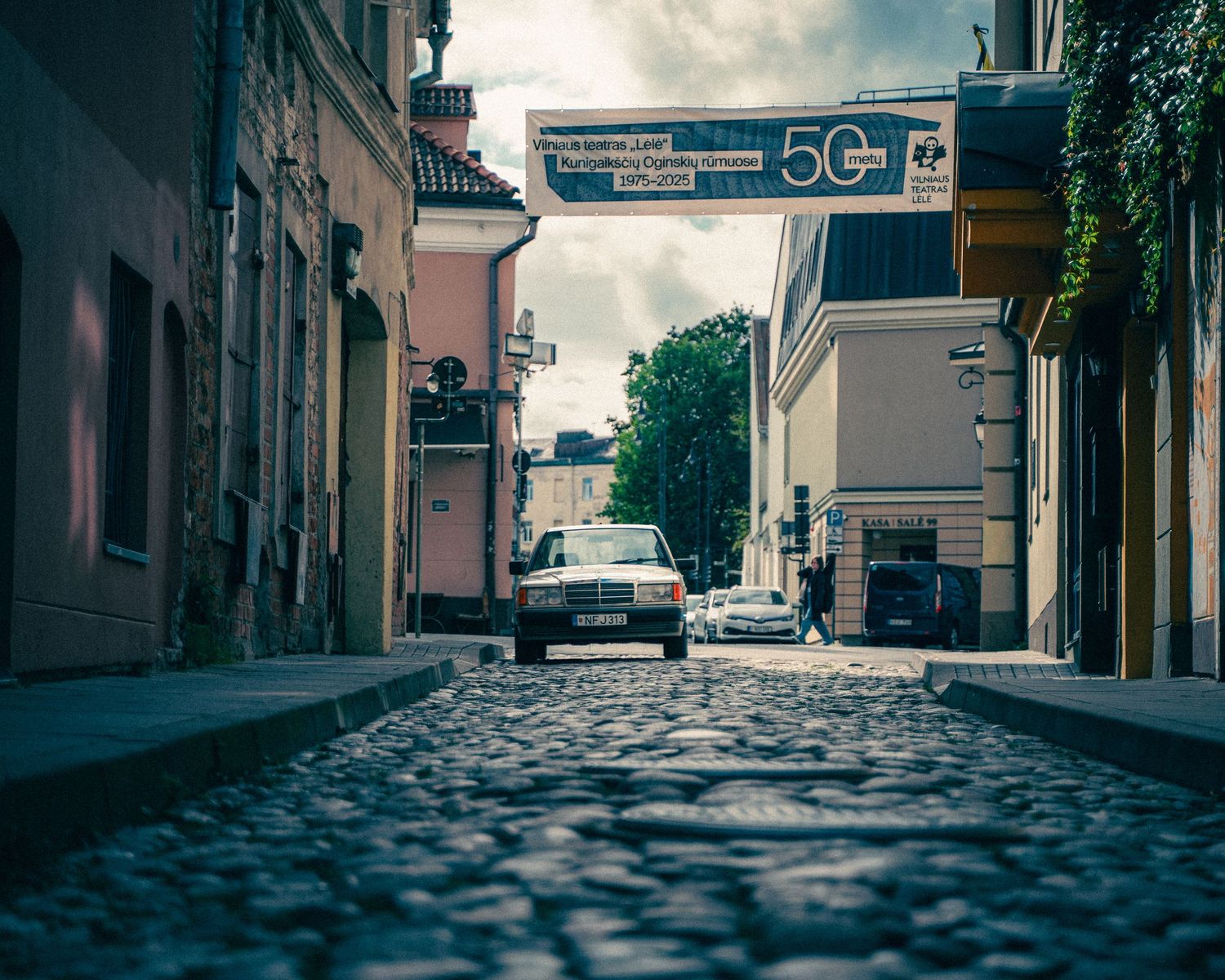 Empty cobblestone street with historic buildings and 50 sign visible in moody urban setting.