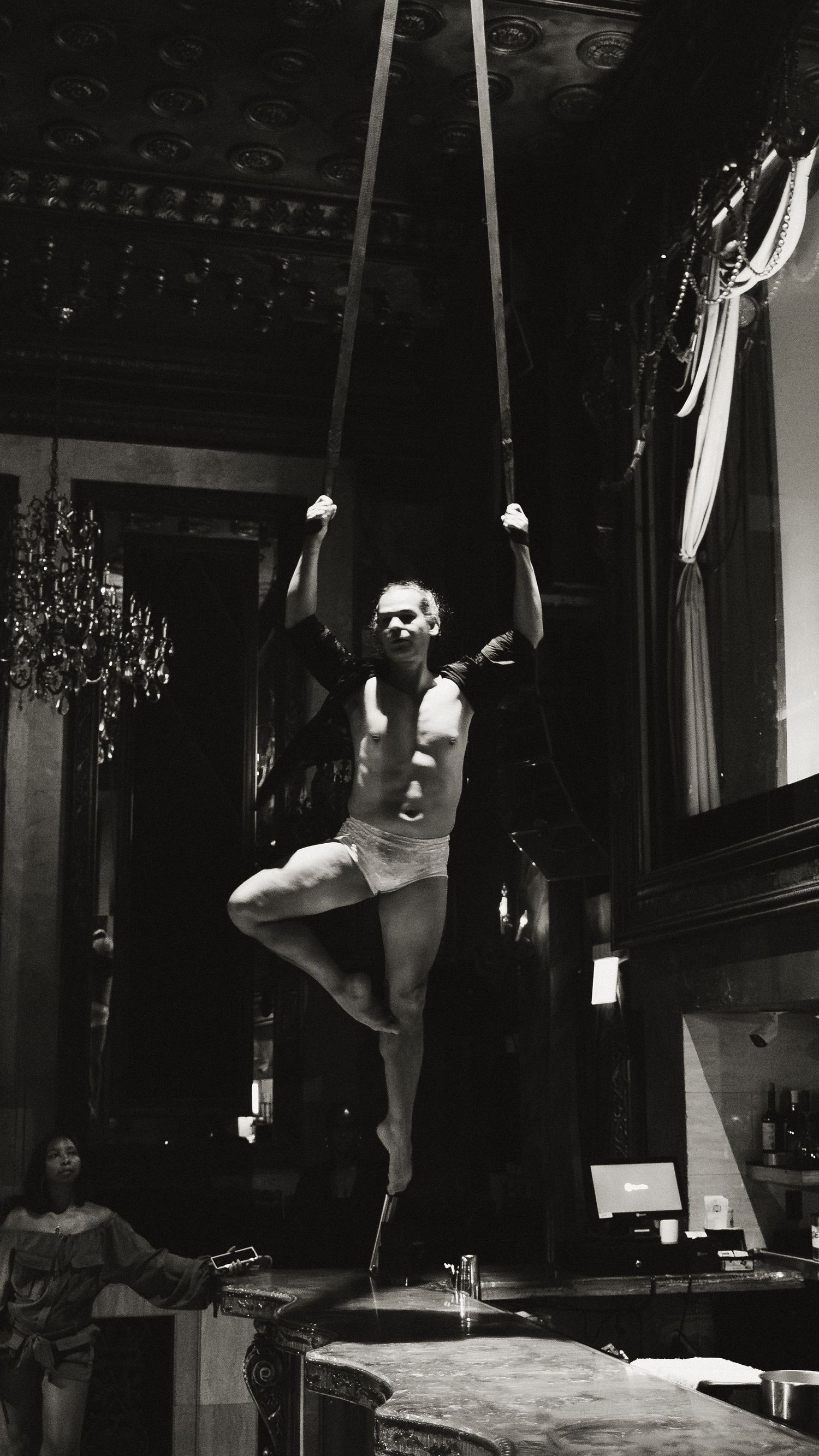Dynamic dance movements captured in black and white against an ornate ceiling with chandeliers.