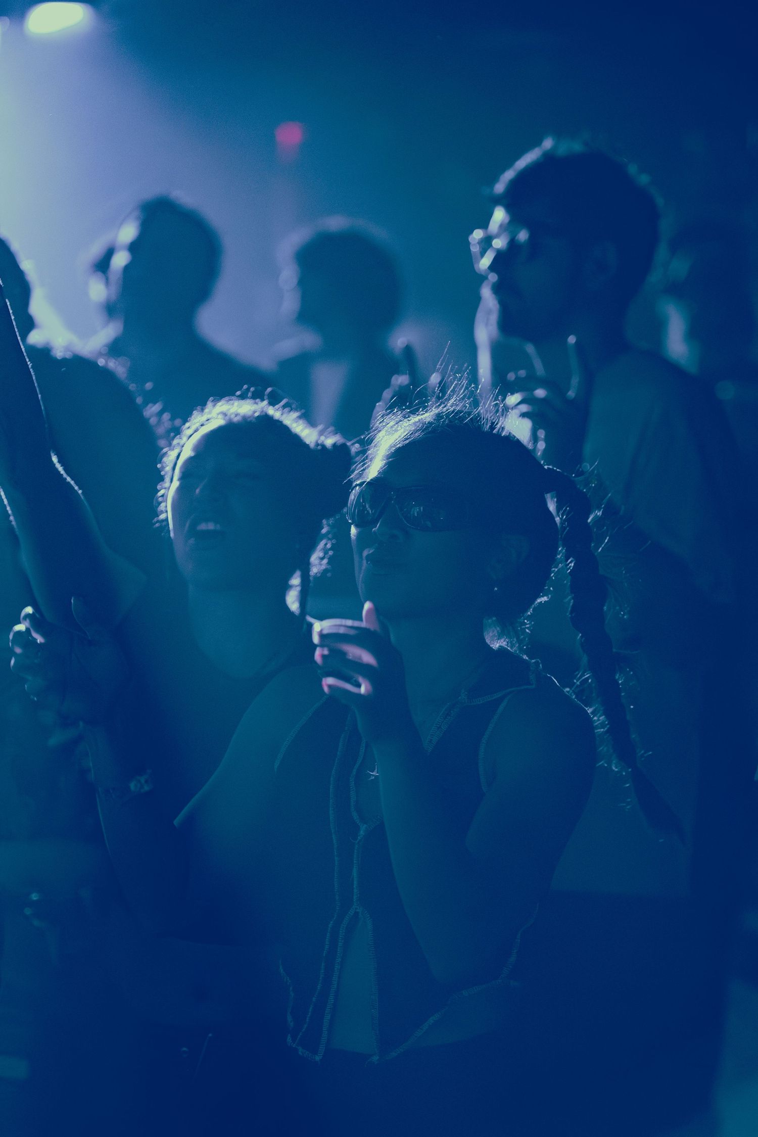 Silhouetted crowd watching a performance in a dimly lit venue with blue atmospheric lighting.