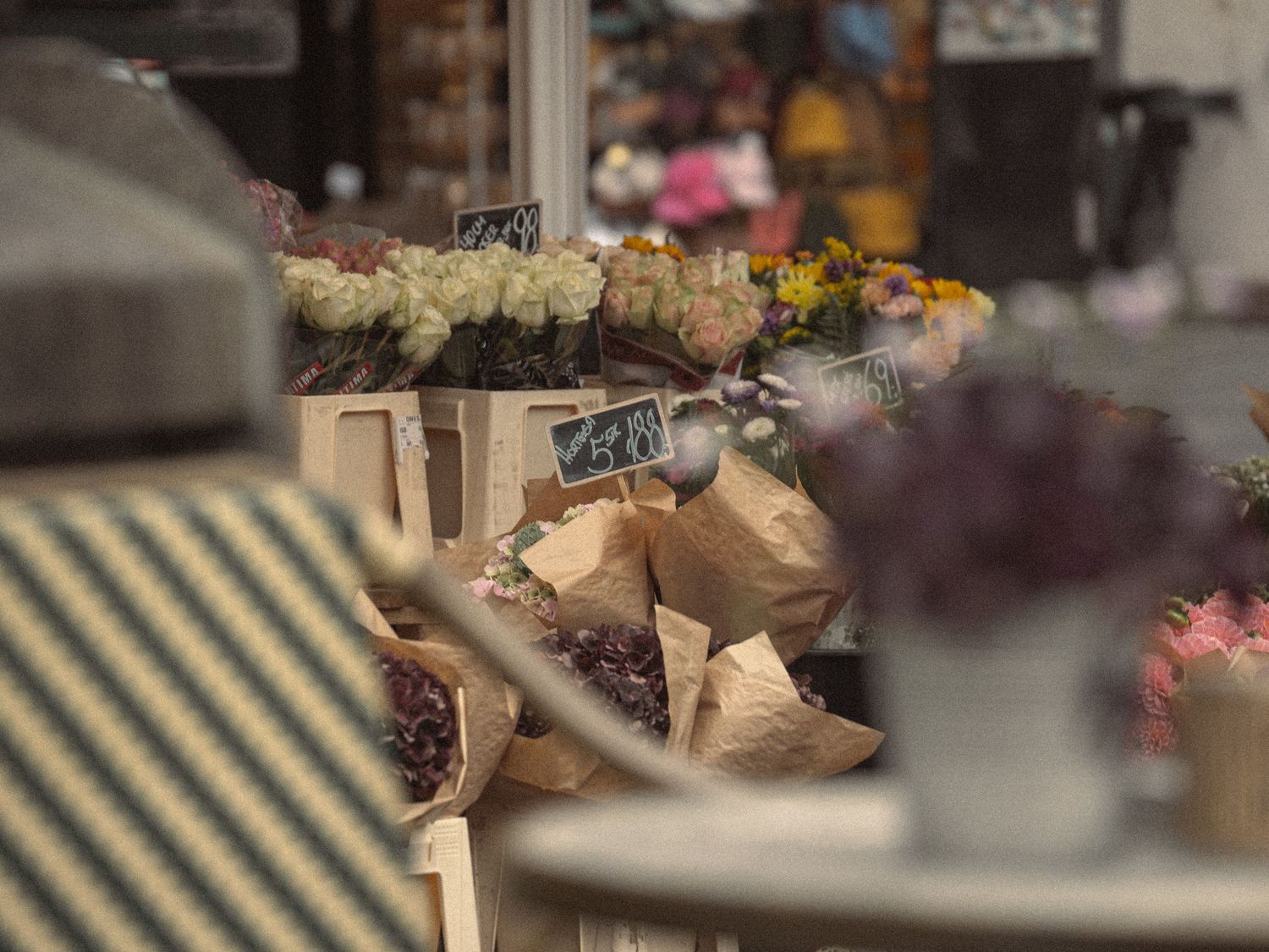 Fresh floral bouquets wrapped in brown paper are displayed at an outdoor market stall with blurred background.
