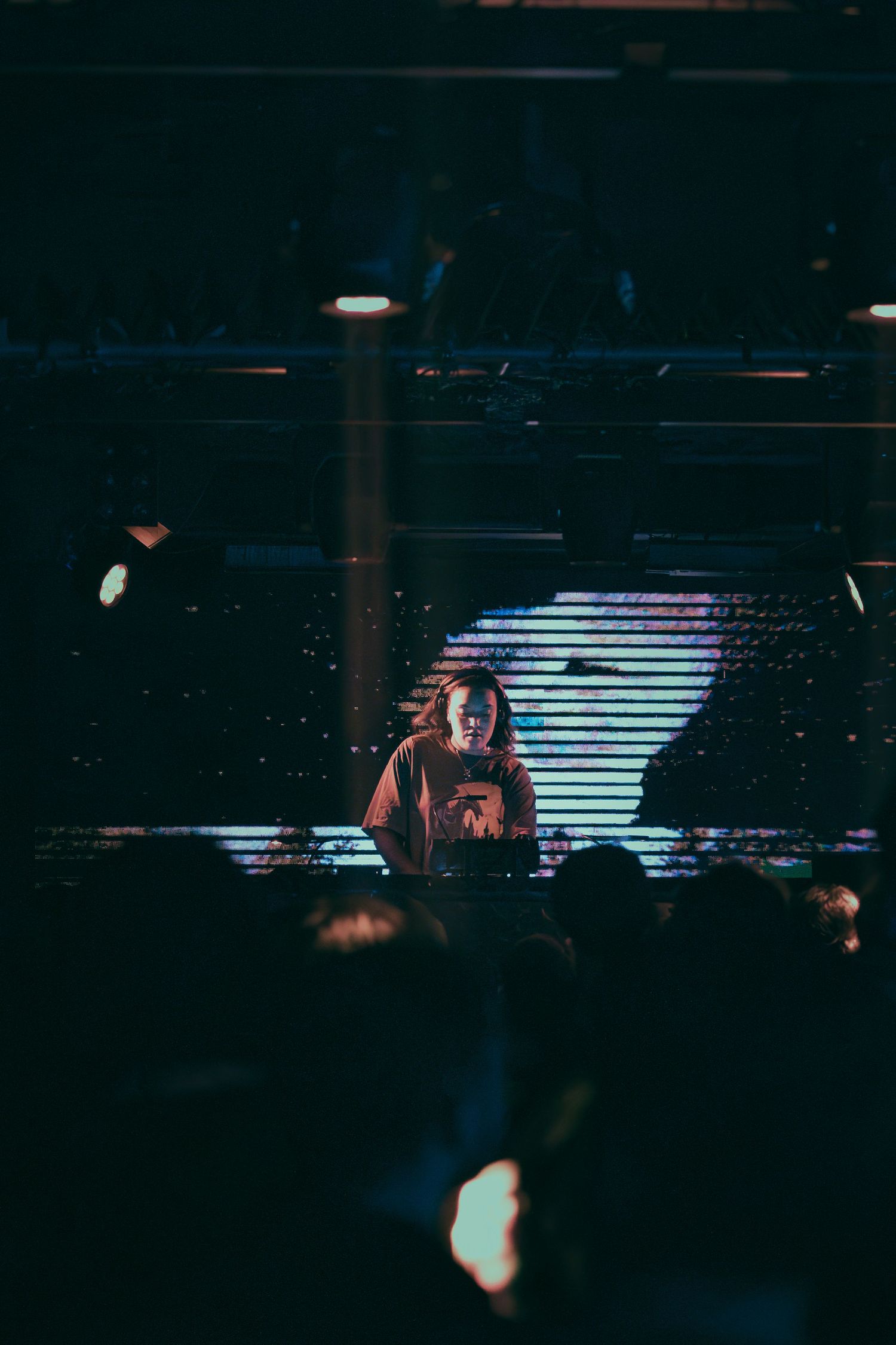 Dark concert venue with illuminated LED screen displays and stage lighting creating atmospheric ambiance.