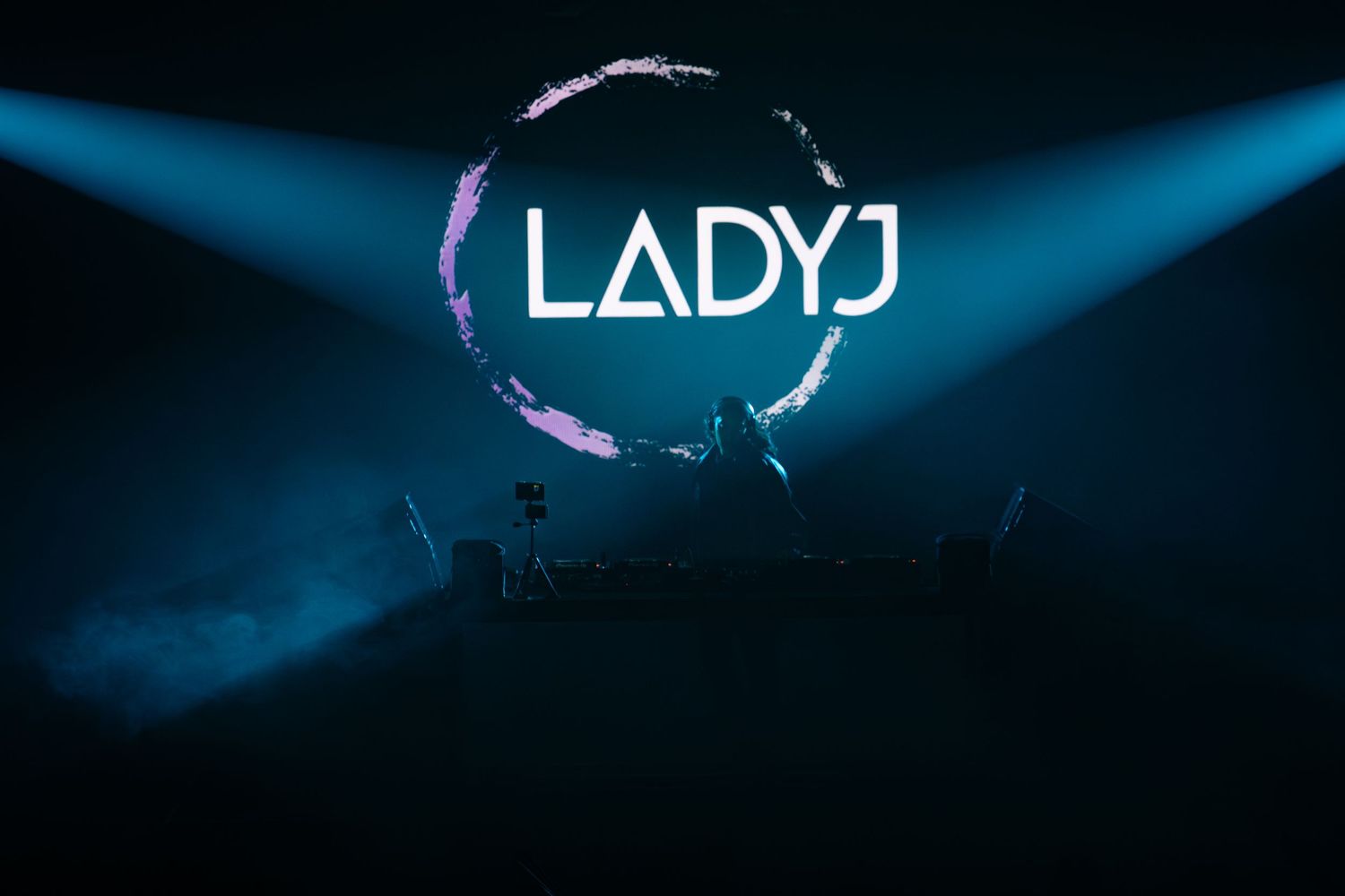 Blue spotlight beams illuminate a dark stage with dramatic lighting effects creating an atmospheric performance space.