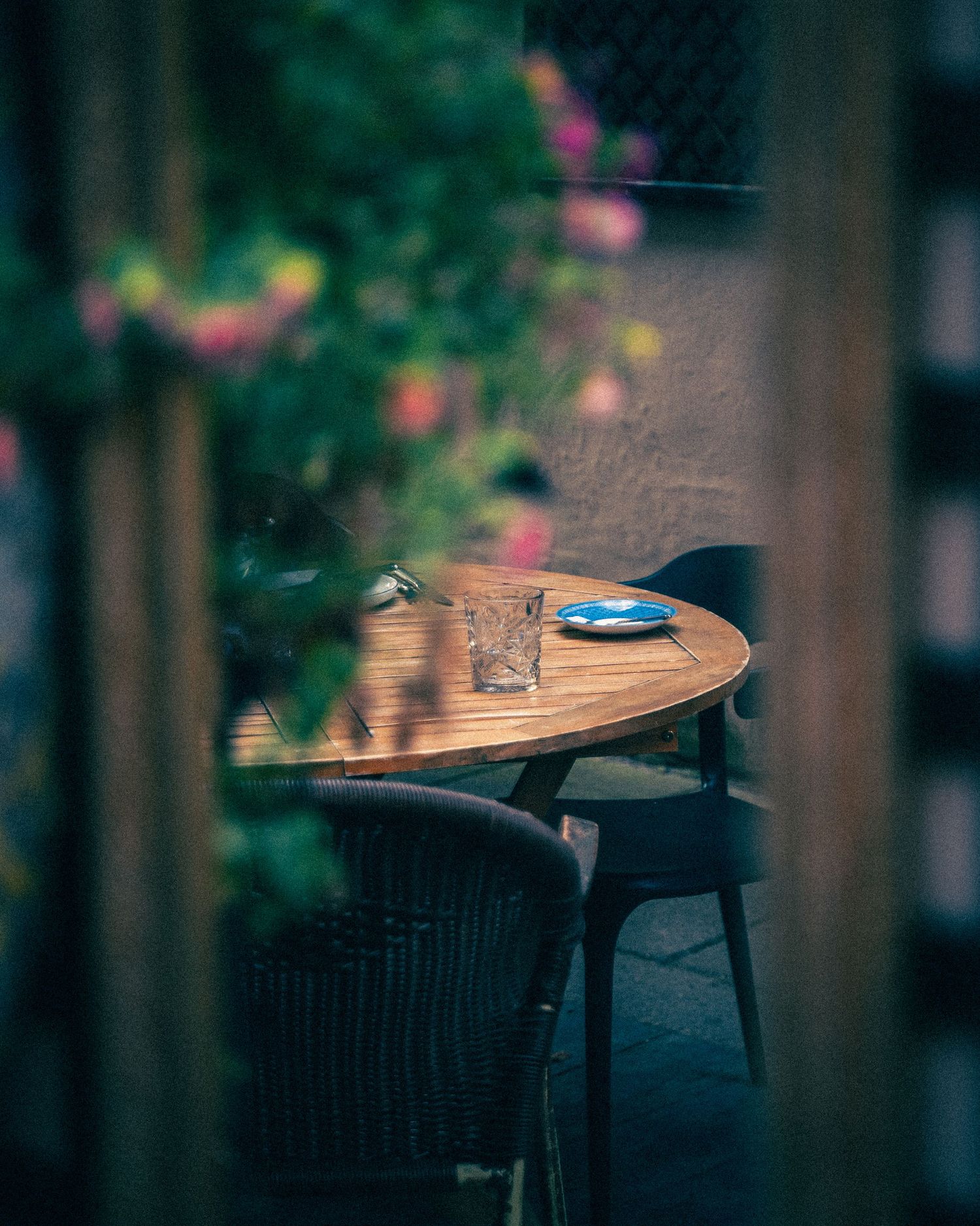 Wooden tables and chairs at outdoor cafe with blurred garden background.