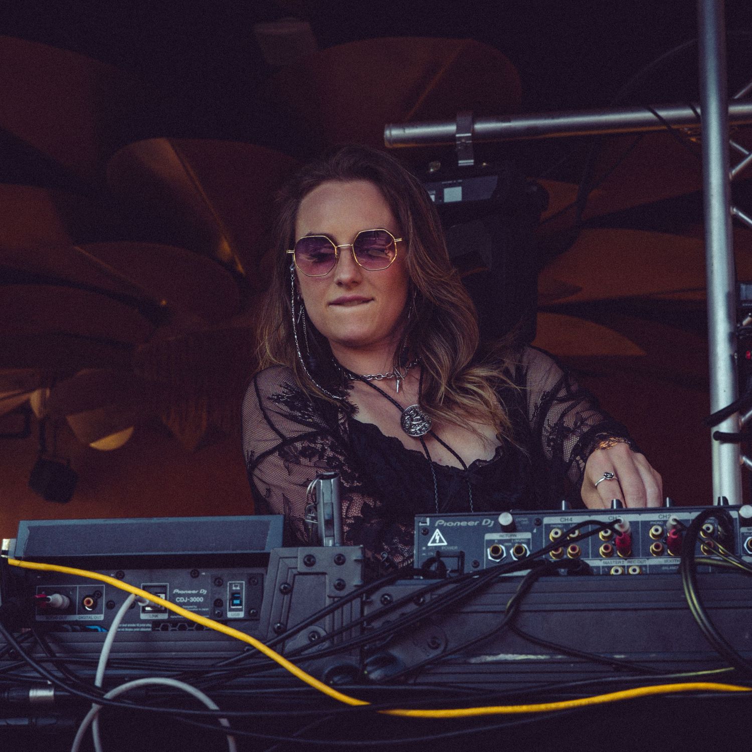 DJ performs at a nightclub behind professional mixing equipment wearing sunglasses and dark attire.