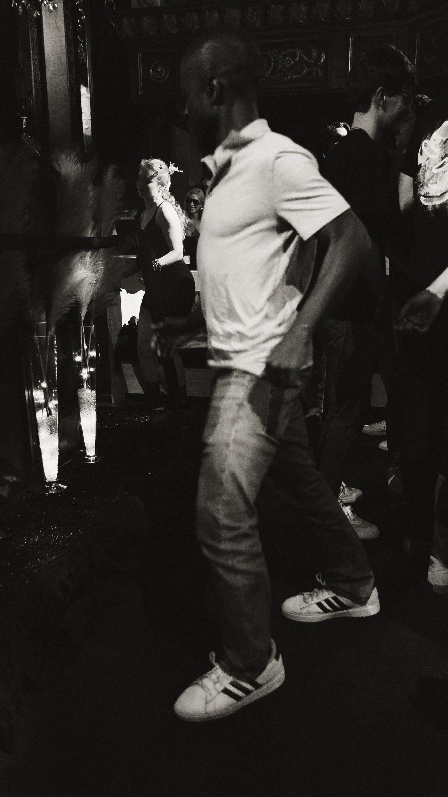 Person in casual attire and sneakers standing in a dimly lit club environment.