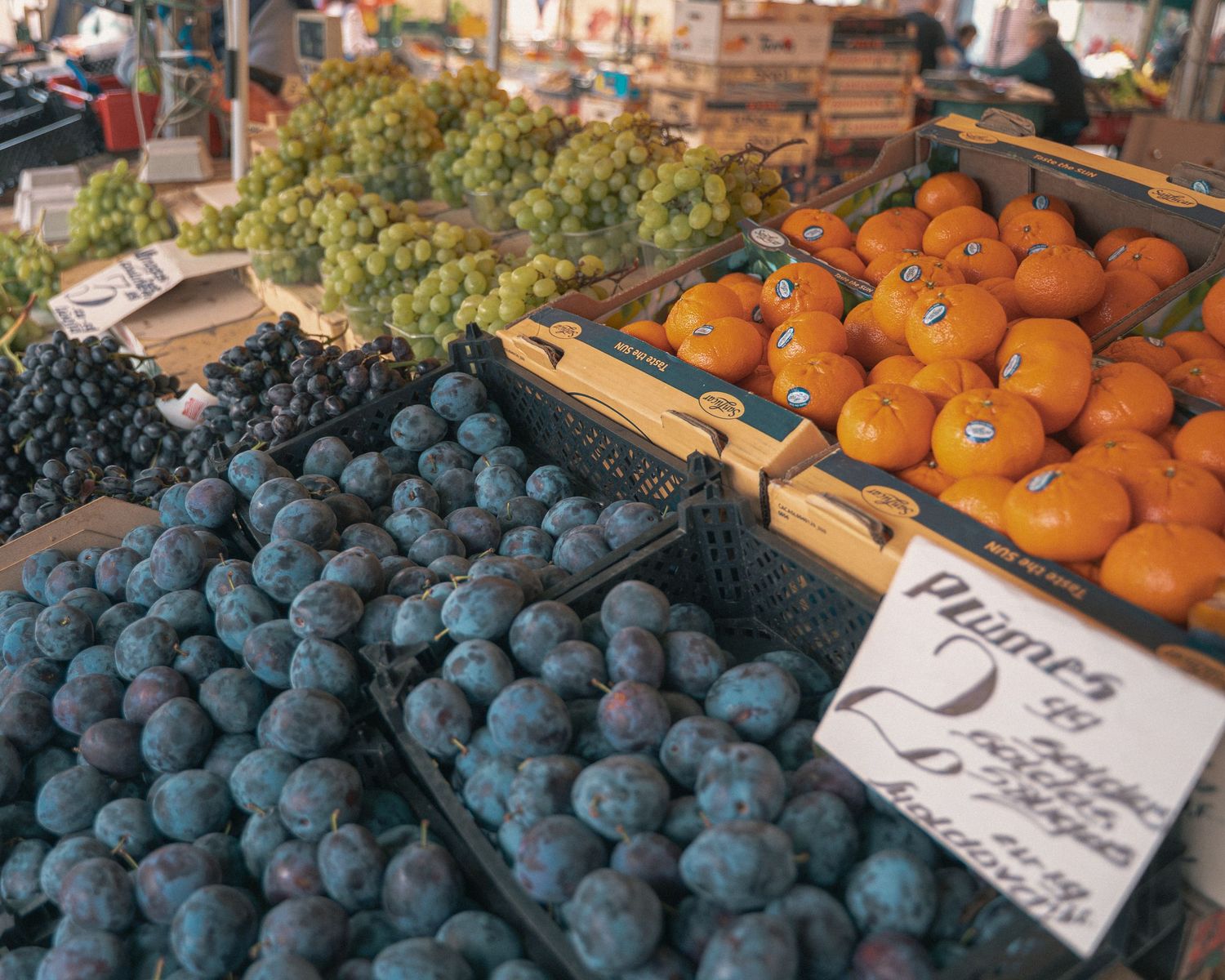 Fresh plums and oranges with price tags displayed at market stall.