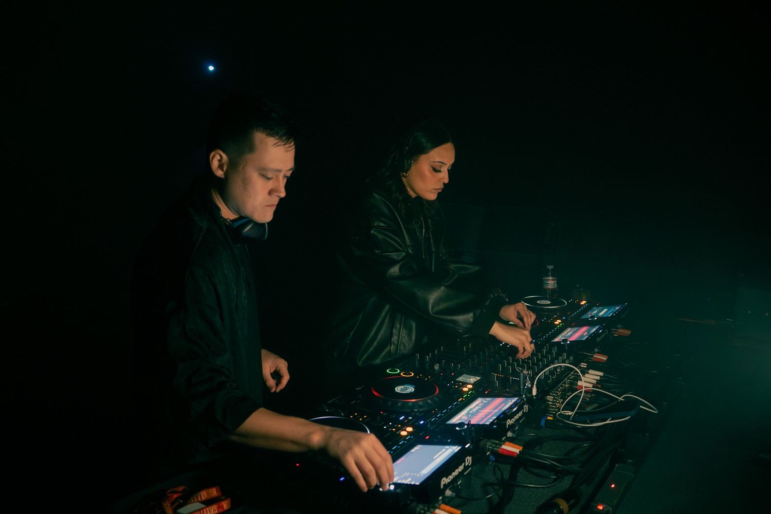 Two people working in a dark room with electronic devices glowing in low-light conditions.