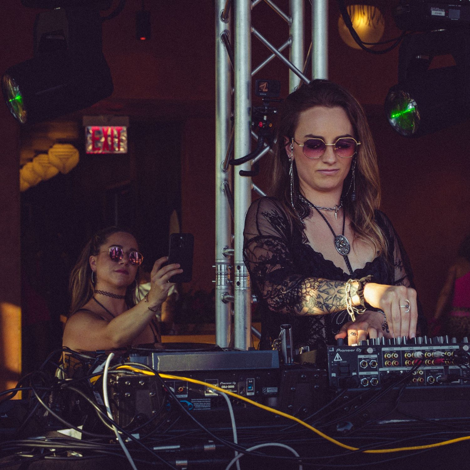 DJ working the mixer controls at a dimly lit nightclub with stage lighting visible.