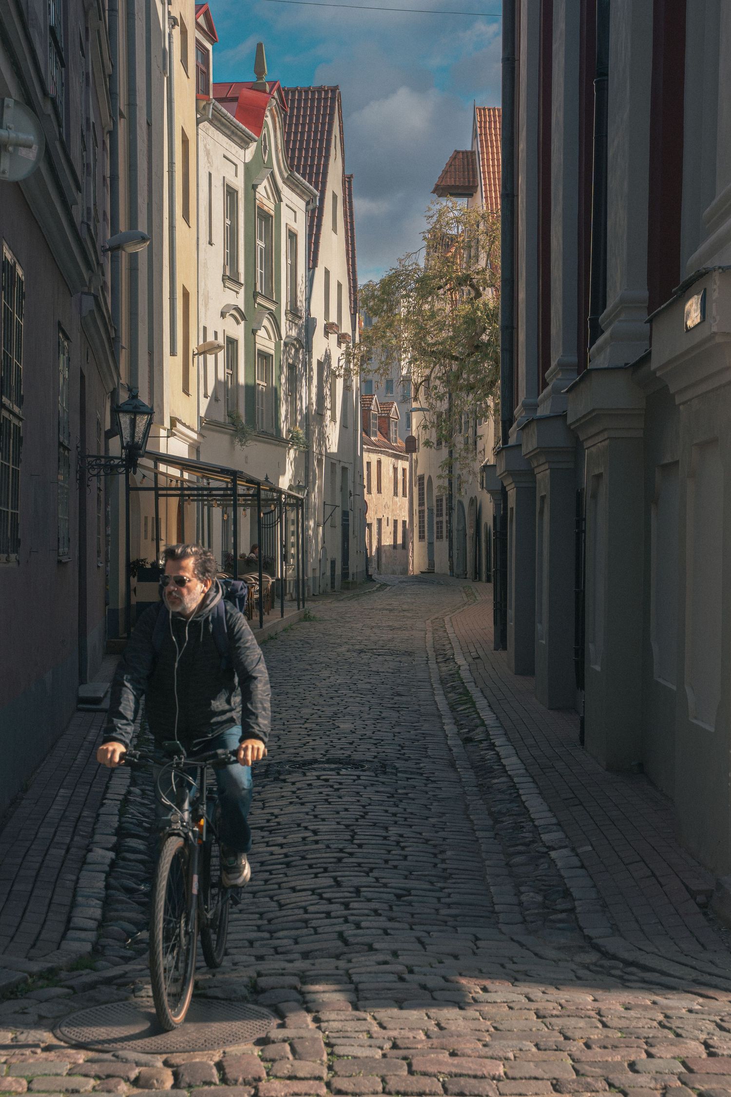 Cobblestone street lined with historic buildings and a lone cyclist in warm sunlight.