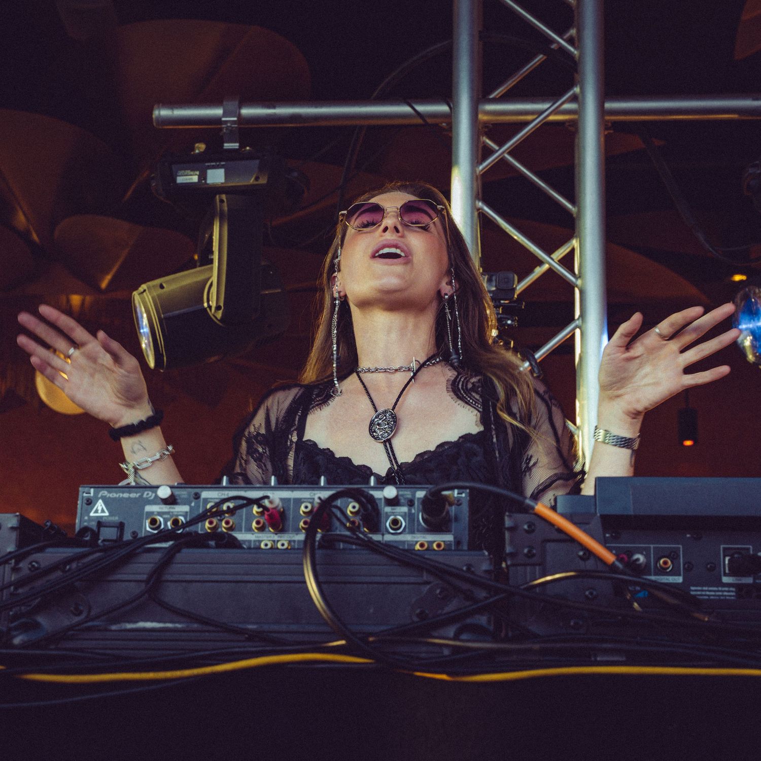 Energetic DJ performance moment with hands raised at club mixing station.