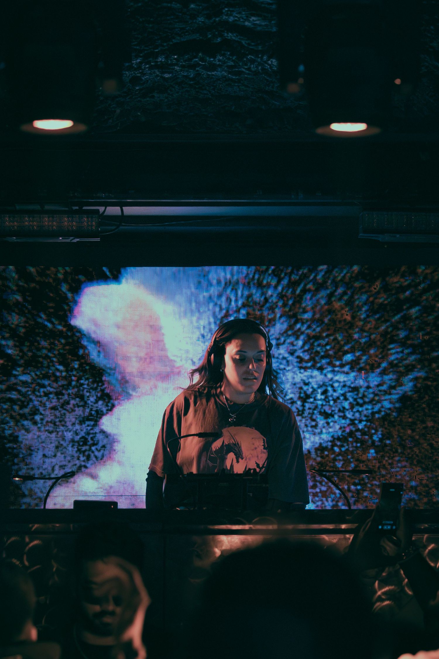 DJ performing at a dark nightclub with colorful lighting effects in the background.